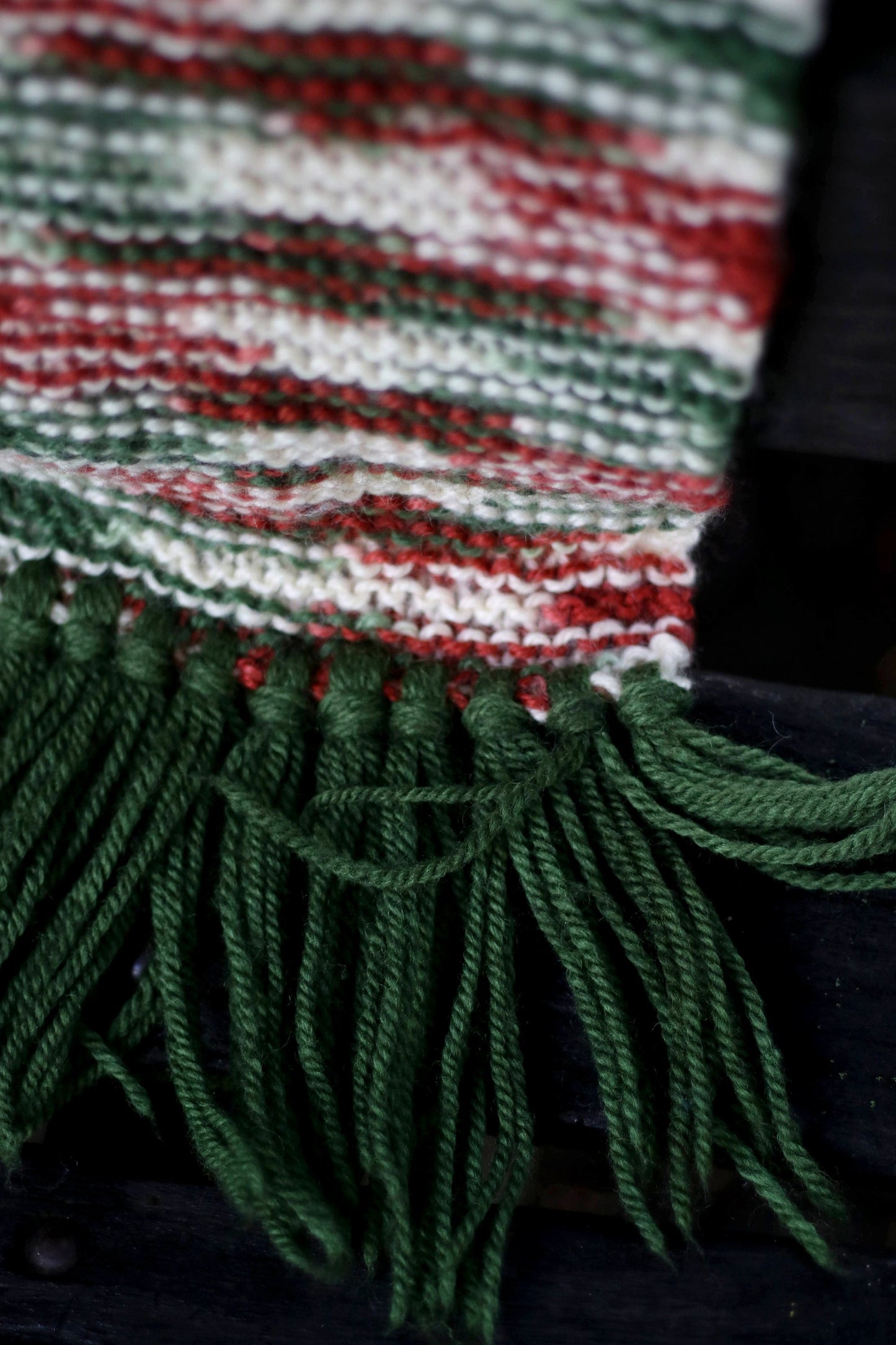 close-up of a Unisex boho knit scarf with long tassels and a warm, chunky feel, the focus is on the texture, the green and red hues and the tassels