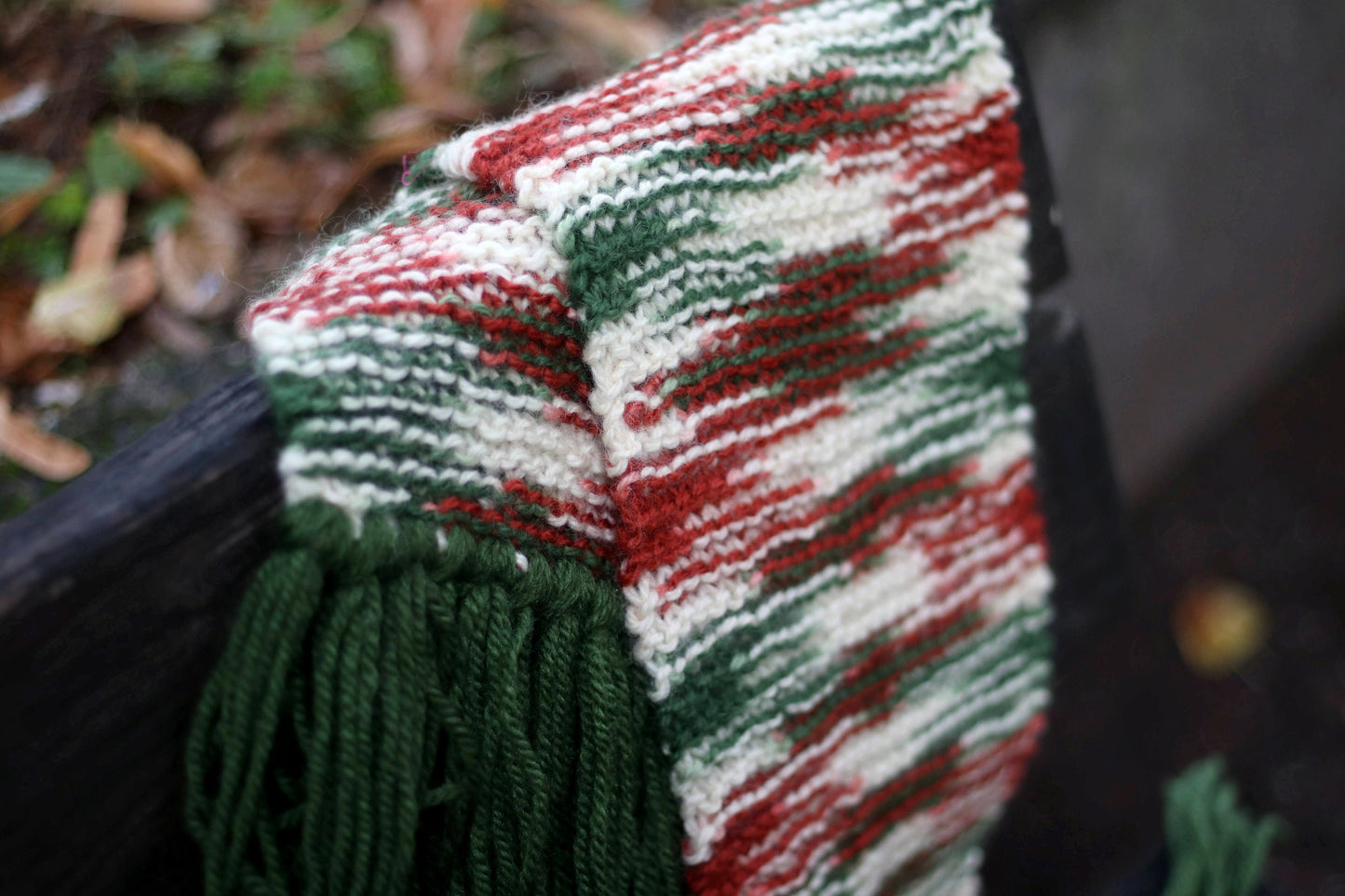 Colorful handmade scarf with statement tassels and a retro vibe, perfect for cold weather fashion phograhed on a wooden surface outdoors with blurred greenery in the background