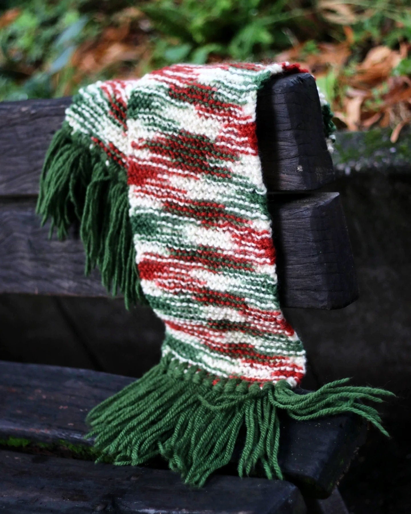 Maximalist winter scarf featuring bold green fringe and a cozy chunky knit texture shot handing on the arm of a wooden bench outdoors with browning leaves blurred on the background