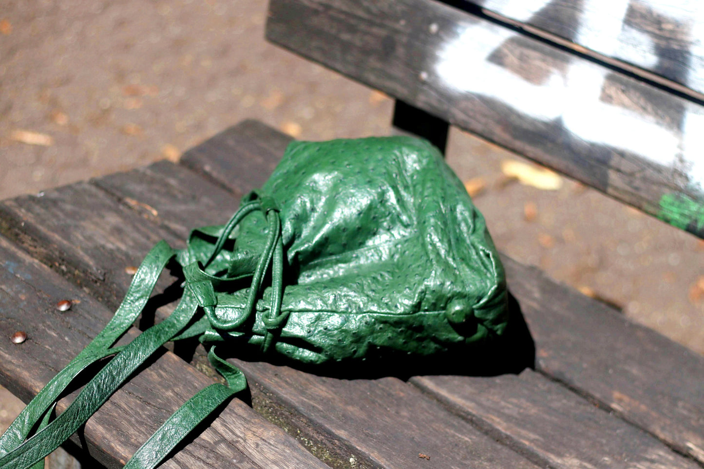 Vintage green bucket drawstring shoulder bag photographed on a park bence. The leather bag is fashionable and of high quality