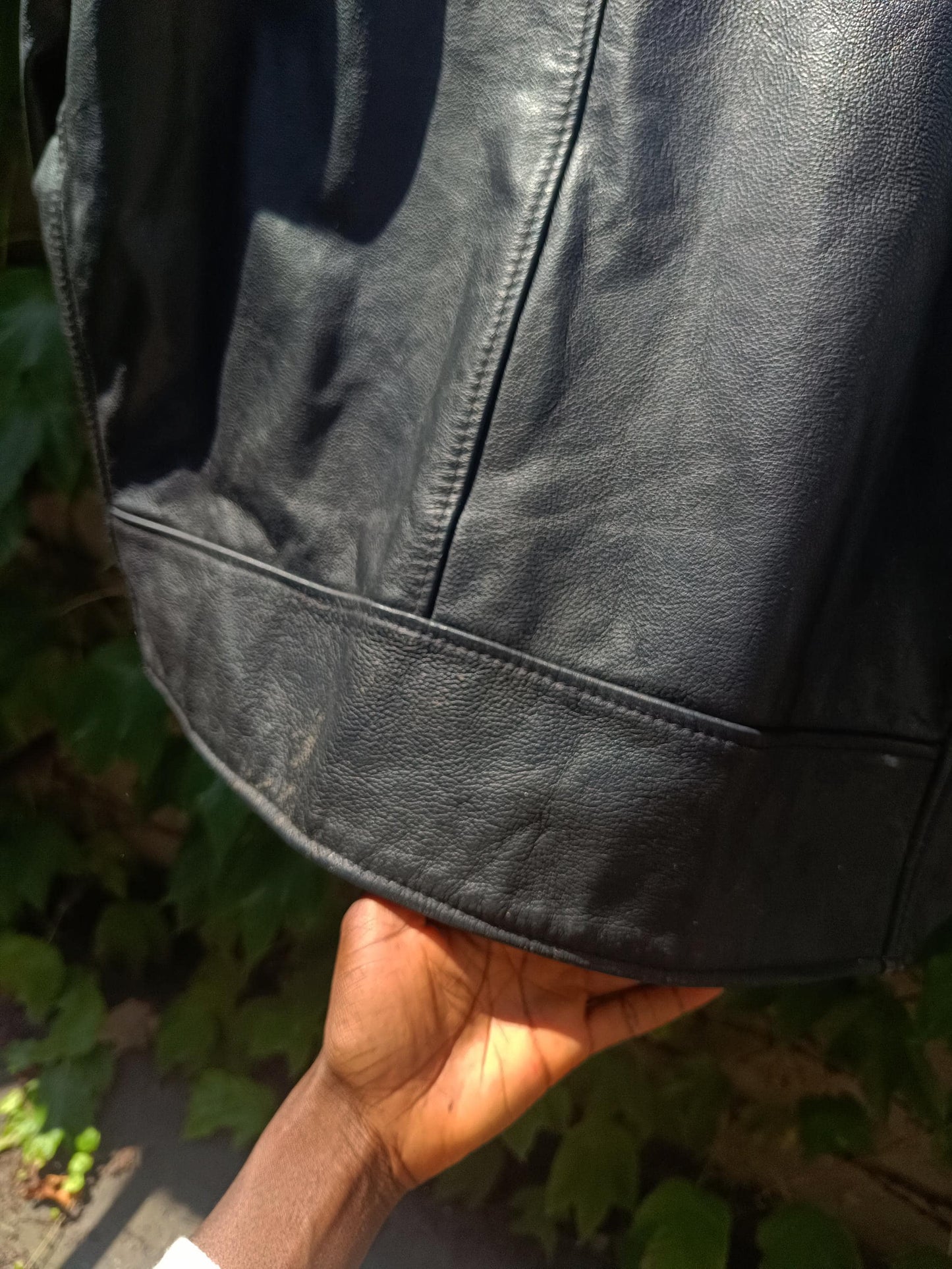 Close up of the bottom part of a vintage black Leather Jacket by the brand Excelled photographed. The photo shows some wear to the jacket from age.