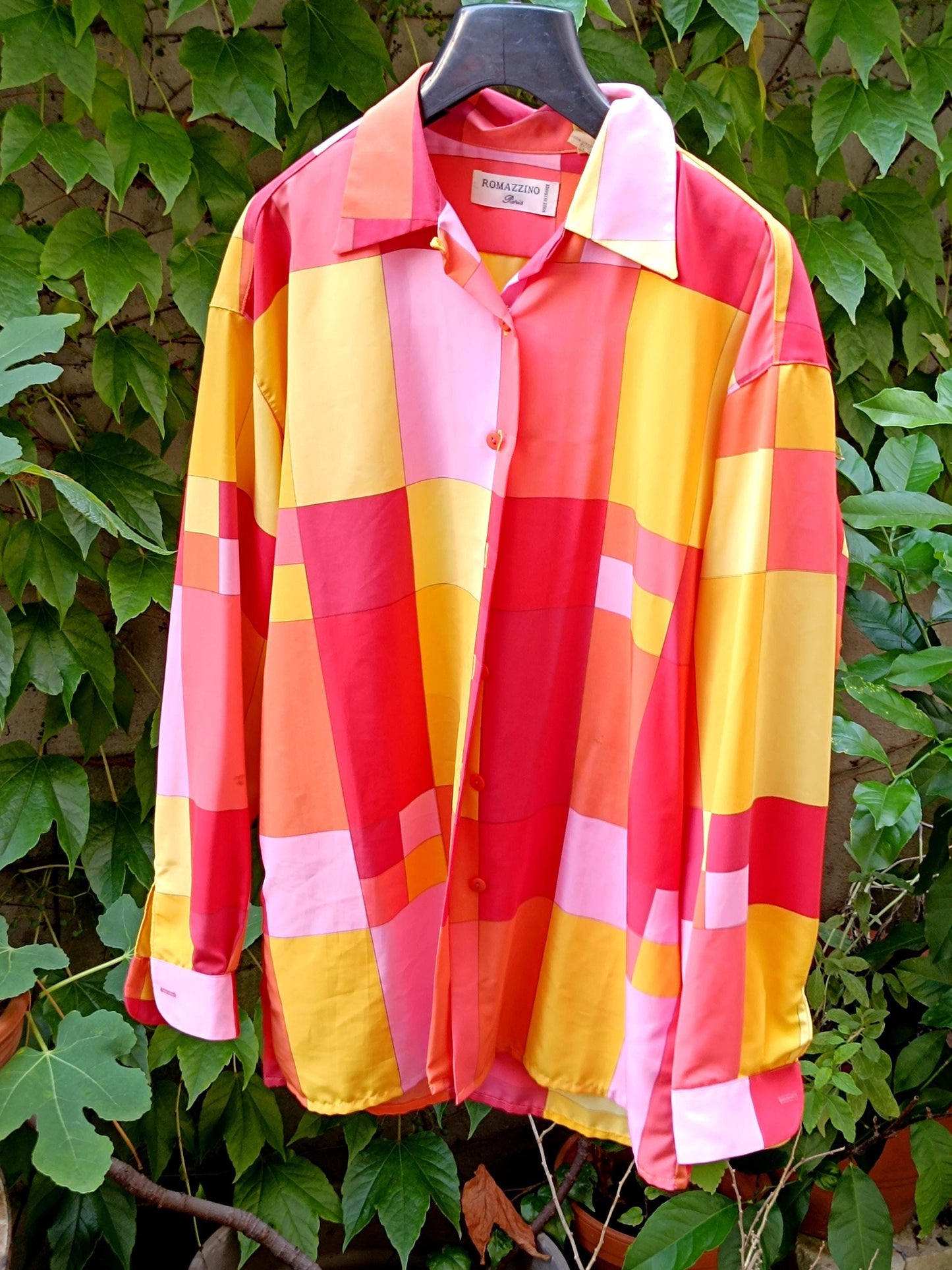 Vibrant 80s checkered blouse with shades of red, pink, yellow, and orange photographed against a green leafy background