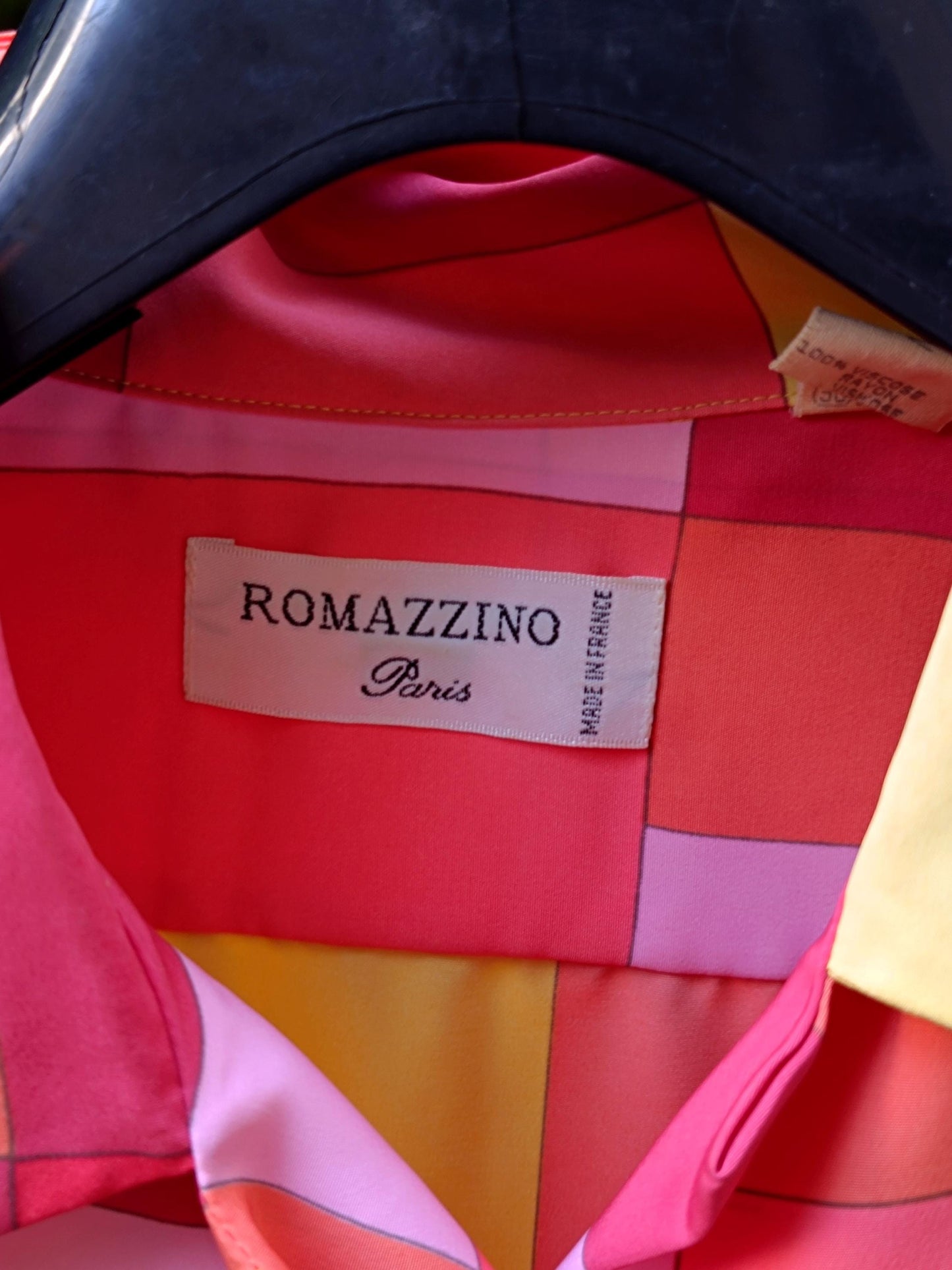 Close up of the label of a vibrant 80s checkered blouse with shades of red, pink, yellow, and orange. The label reads Romazzino Paris.
