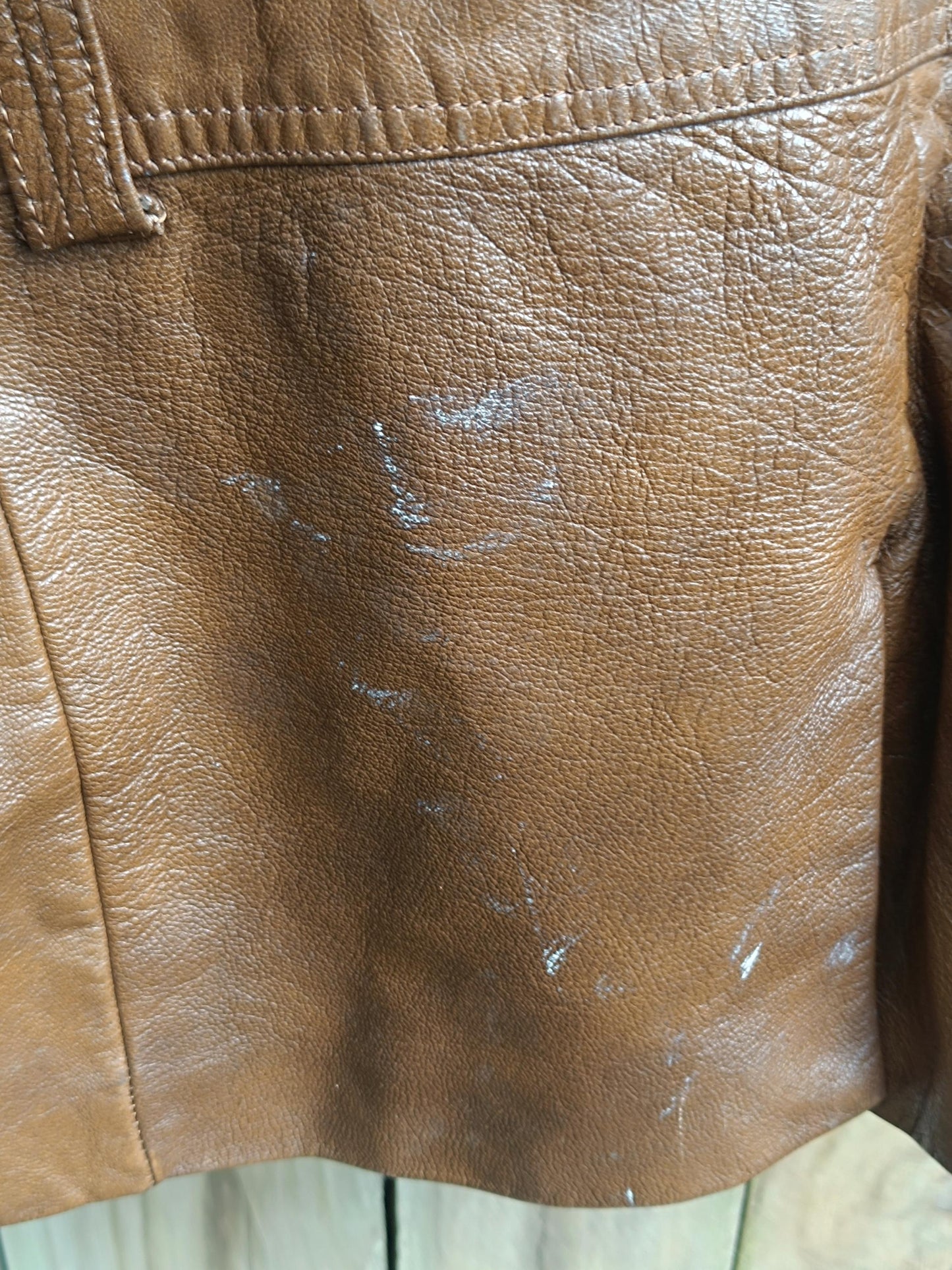 A close-up photo of the white stain on a vintage 90s leather Jacket in brown is. The image highlights the extent of the minor stain