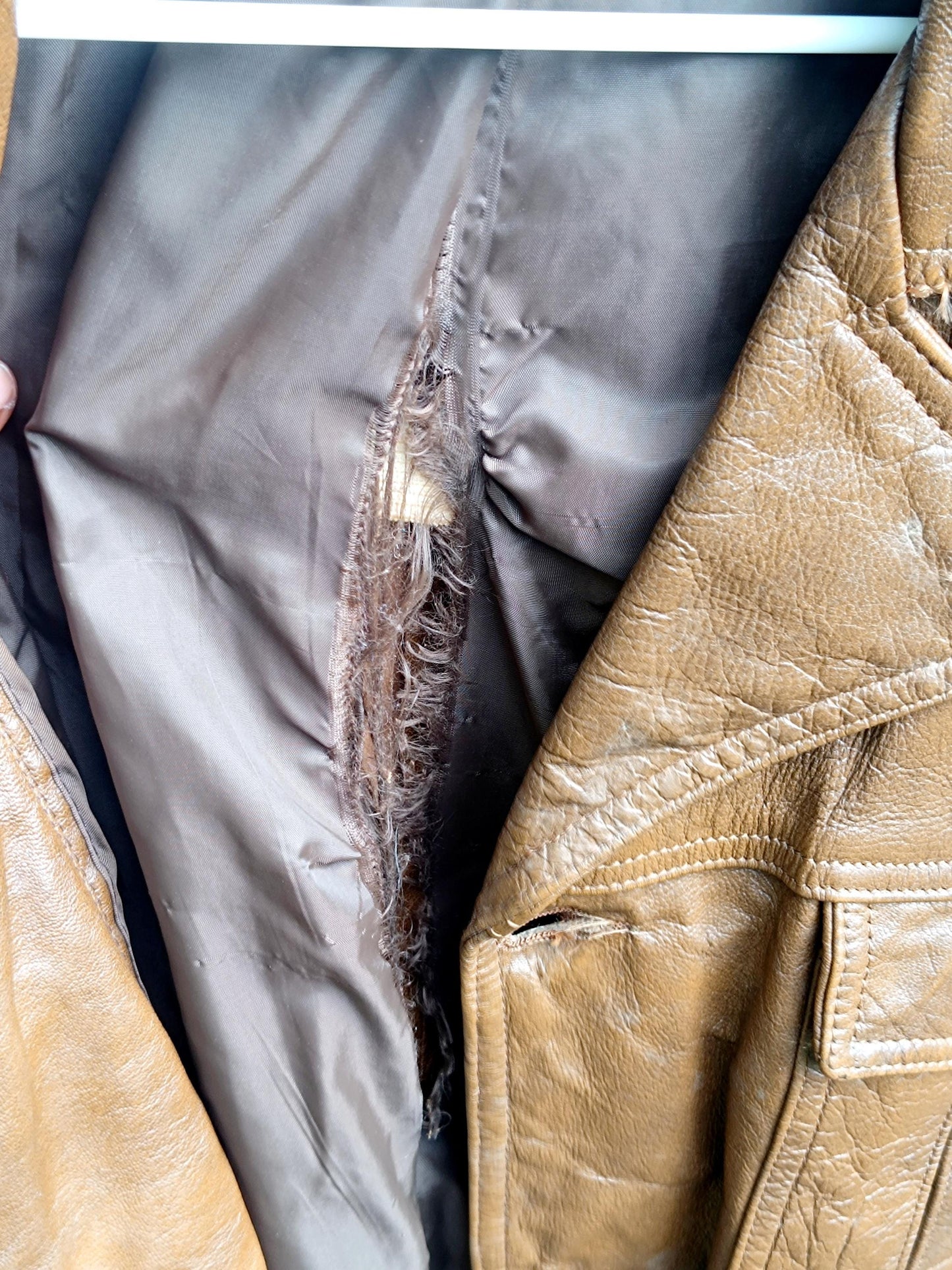 A detailed shot of the lining of a Vintage 90s Leather Jacket in brown. The image focuses on the tear in the lining