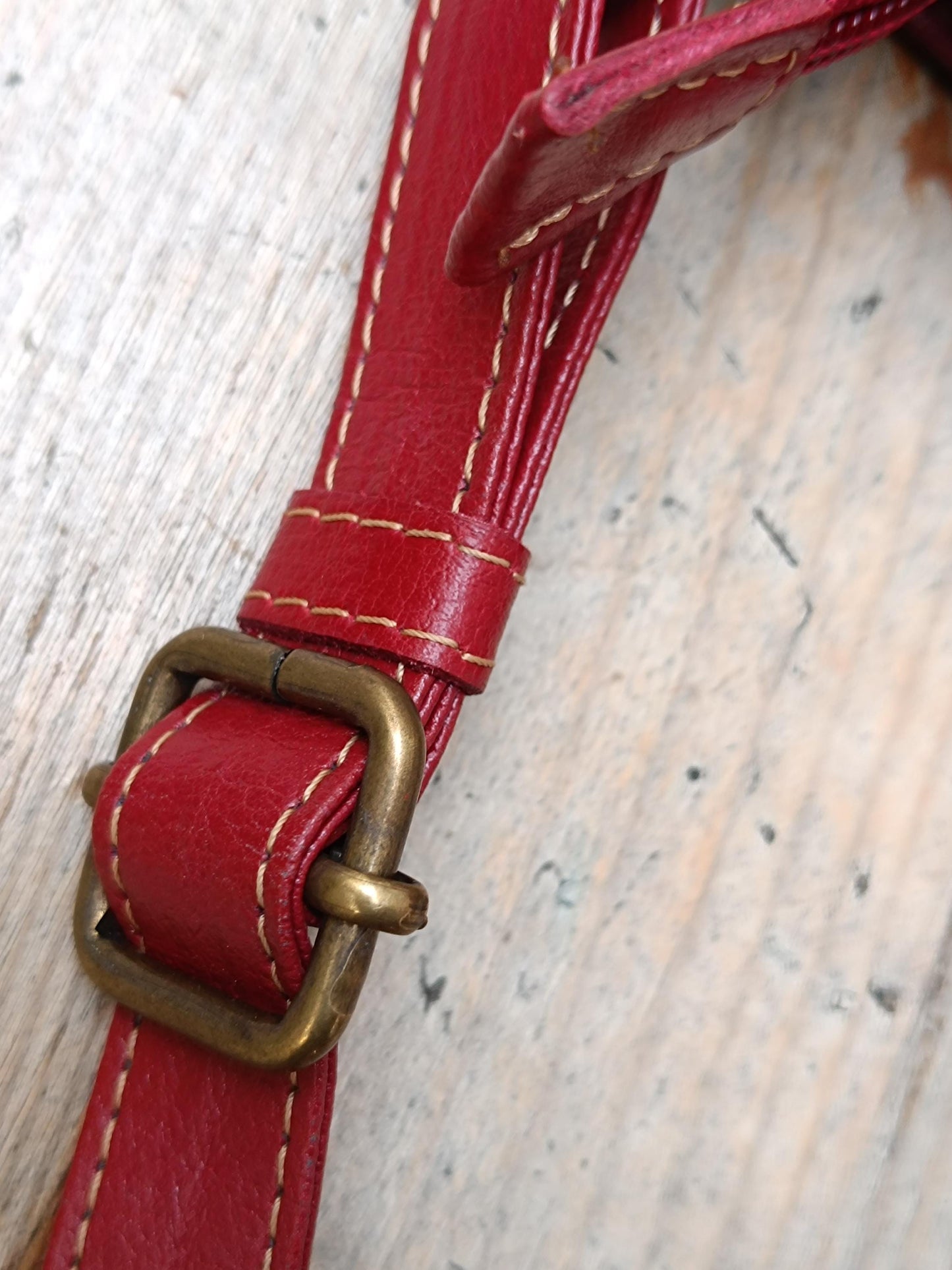 the strap of a red leather shoulder bag is displayed on a light-colored wooden chair. The image provides a clear view of the adjustable strap's design, color, and condition.