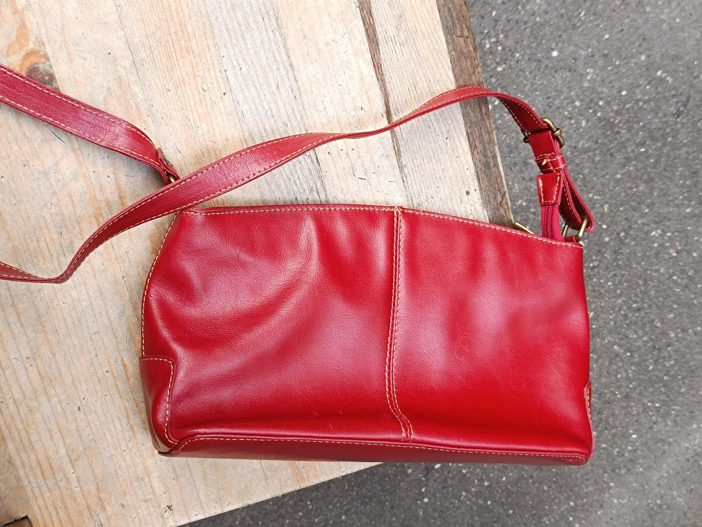 Vintage red leather shoulder bag from the 90snwith a single adjustable strap and silver hardware is displayed on a light wooden chair.