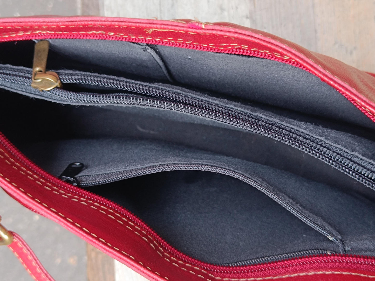 An image of the insides of a vintage red leather shoulder bag photographed on a light-colored wooden chair. The zoomed-in picture provides a clear view of the bag's multiple compartments and colour.