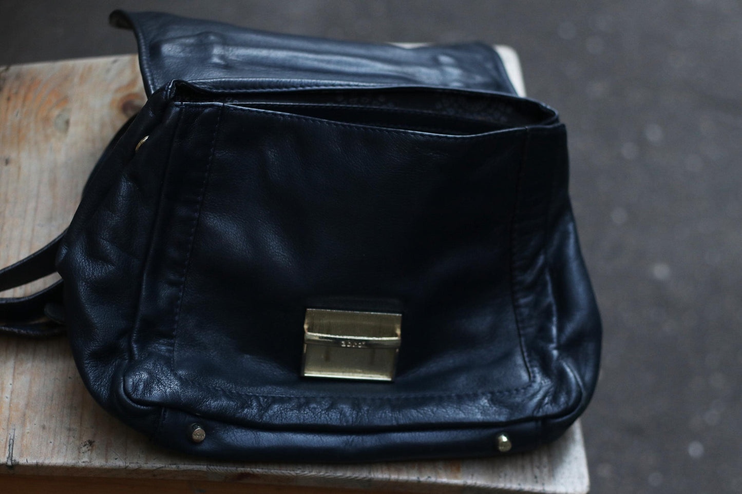 Close-up of an open, vintage black leather shoulder bag on a weathered wooden surface. Focus on the silver-toned clasp and the texture of the aged leather. The bag's interior is visible, showcasing its spaciousness.
