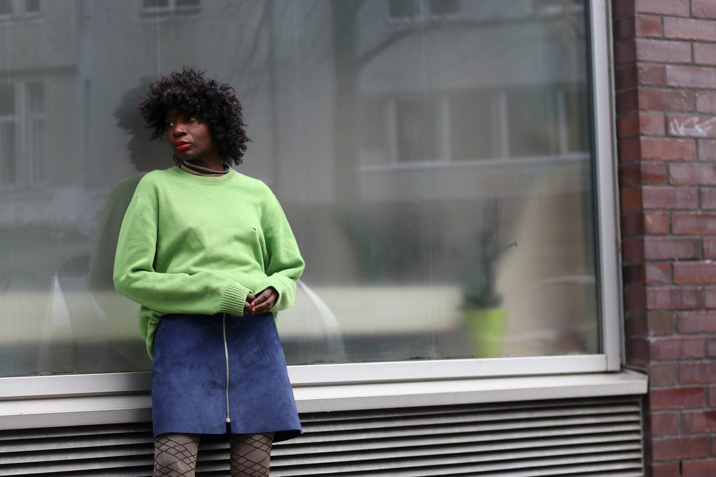 A person wearing a green sweater and a blue denim skirt.