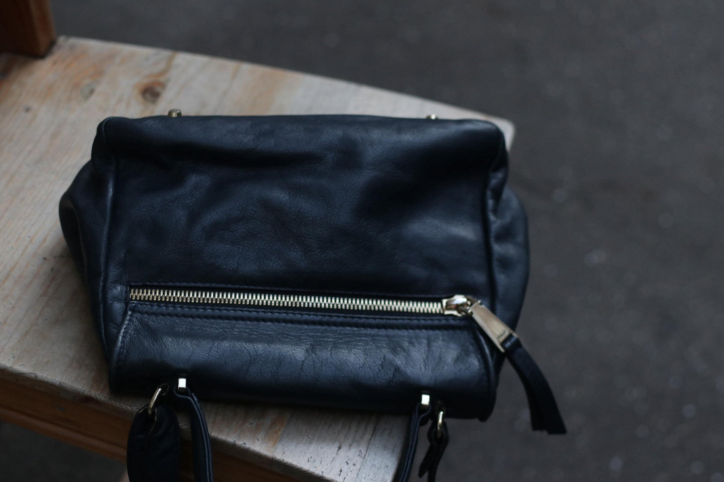 A vintage Black leather top-handle and shoulder bag from the 90s by the brand Abro is captured on wooden surface. the image focuses on the back compartment with a silver-toned zipper