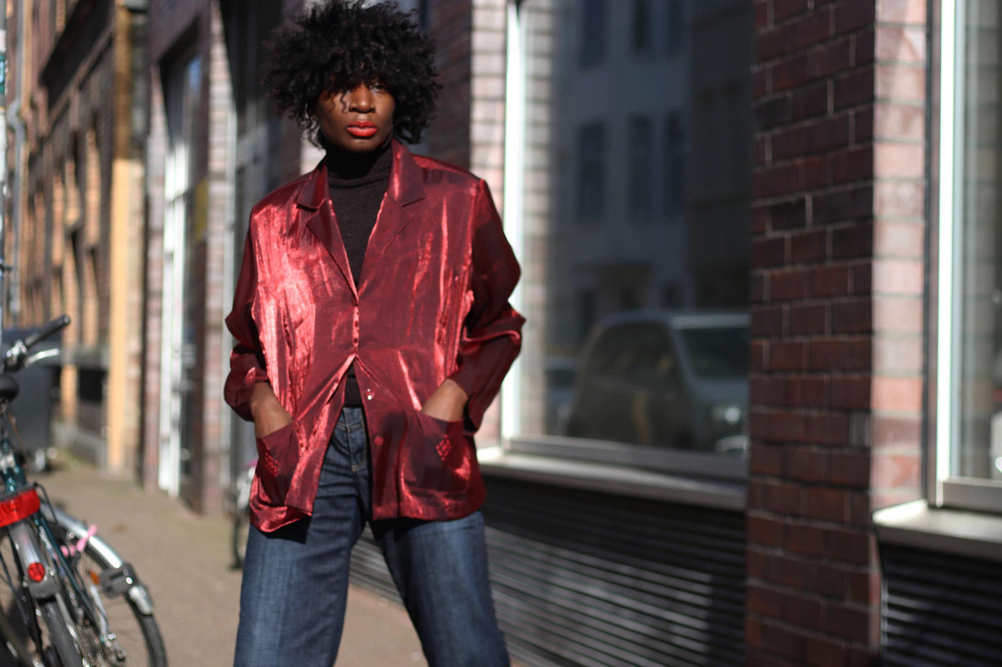A black female wearing a 90s shiny red satin-like blouse with embroidered pockets, styled with wide-leg jeans on a city street.