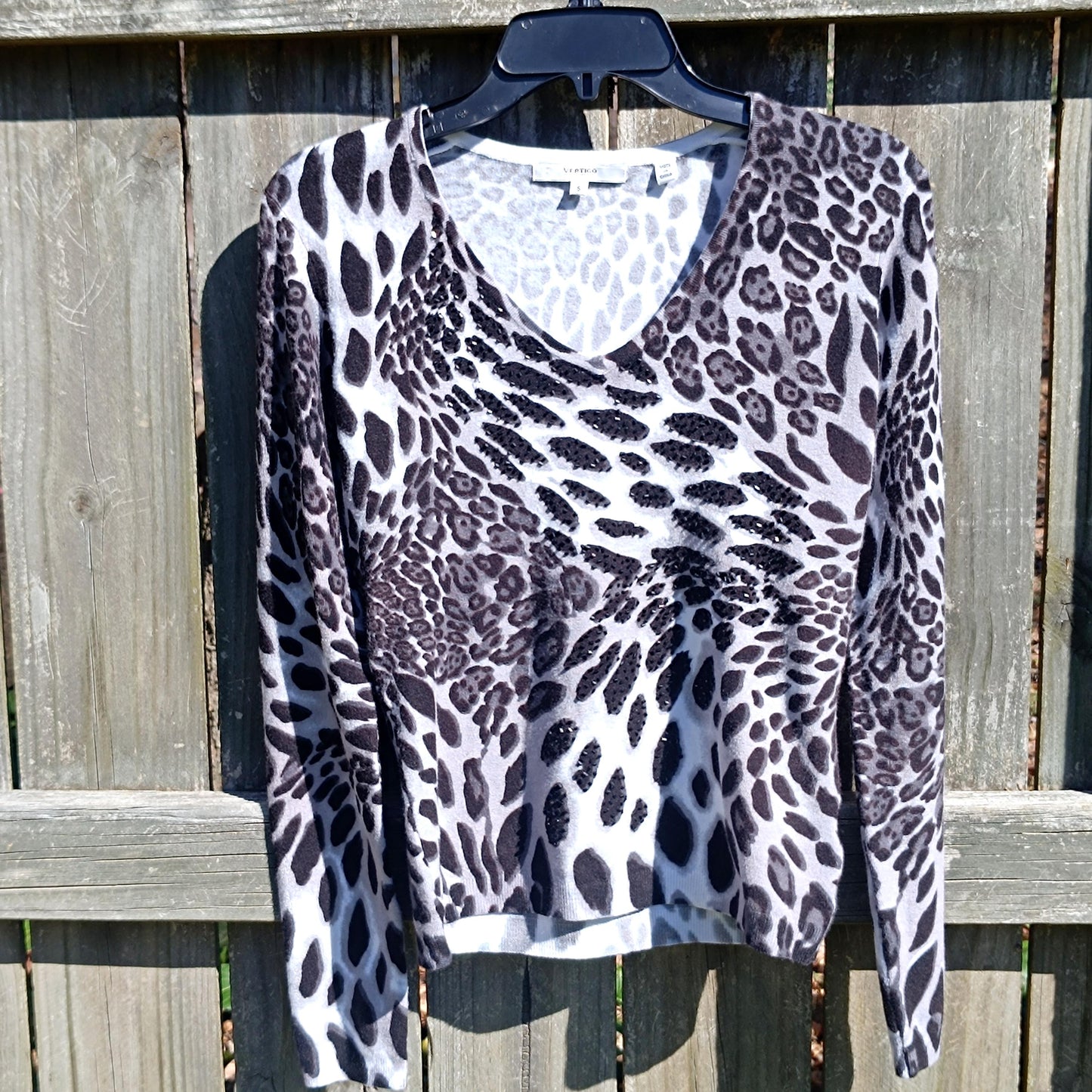 A vintage long-sleeved Vertigo Paris top with a black and white abstract print that resembles animal print hanging against a wooden shed