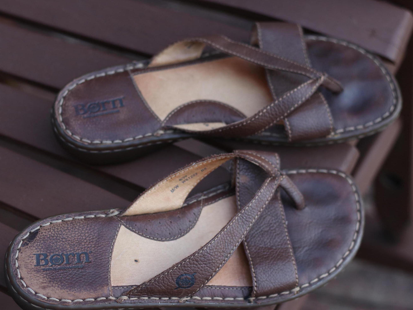 Comfortable handcrafted 90s Børn designer sandals with a relaxed, broken-in aesthetic. The vintage flip flops are photographed on a wooden brown chair outdoors.
