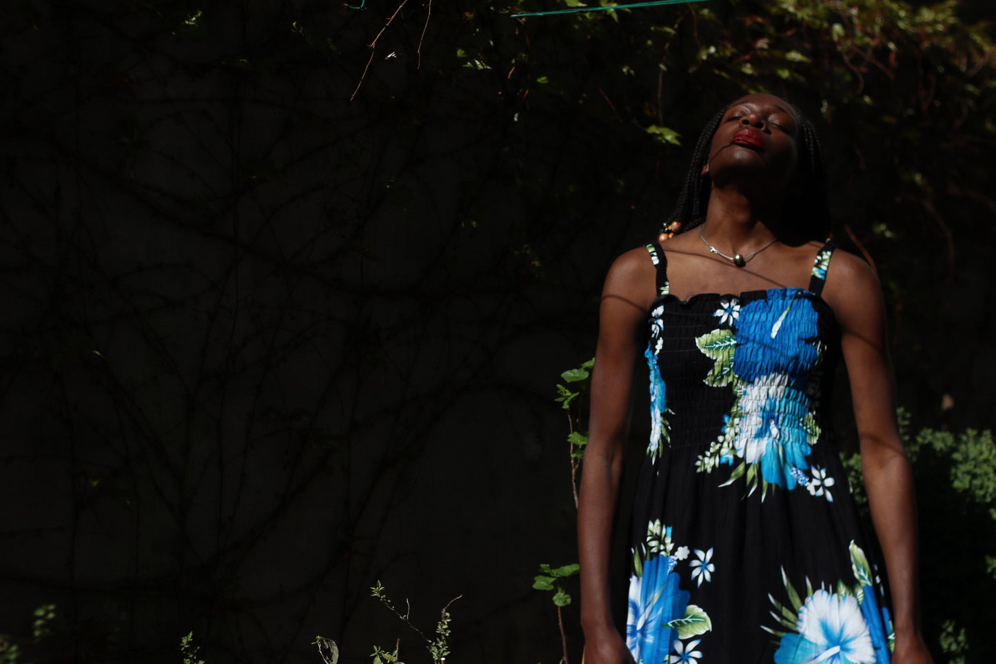 Outdoor fashion shot of a female model wearing a vintage 90s lightweight rayon sundress with a bold black background adorned with oversized blue and white flower patterns. The dress has thin straps and a relaxed, flowing silhouette, giving off an Hawaiian summer vibe.