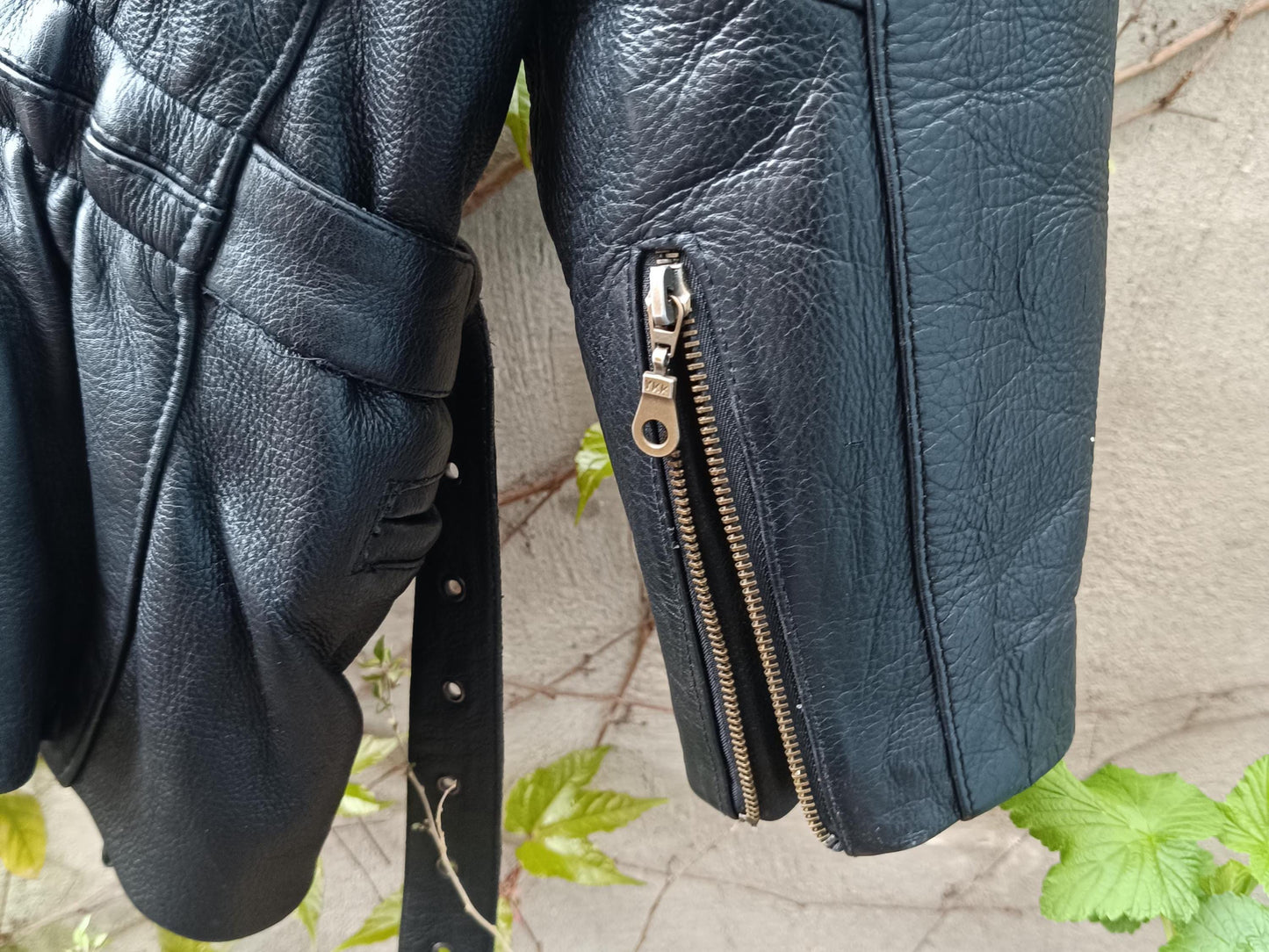 Close-up of a zipper detail on the sleeves of a vintage 80s black leather biker jacket with asymmetrical zipper, belt and rouched drop waist details