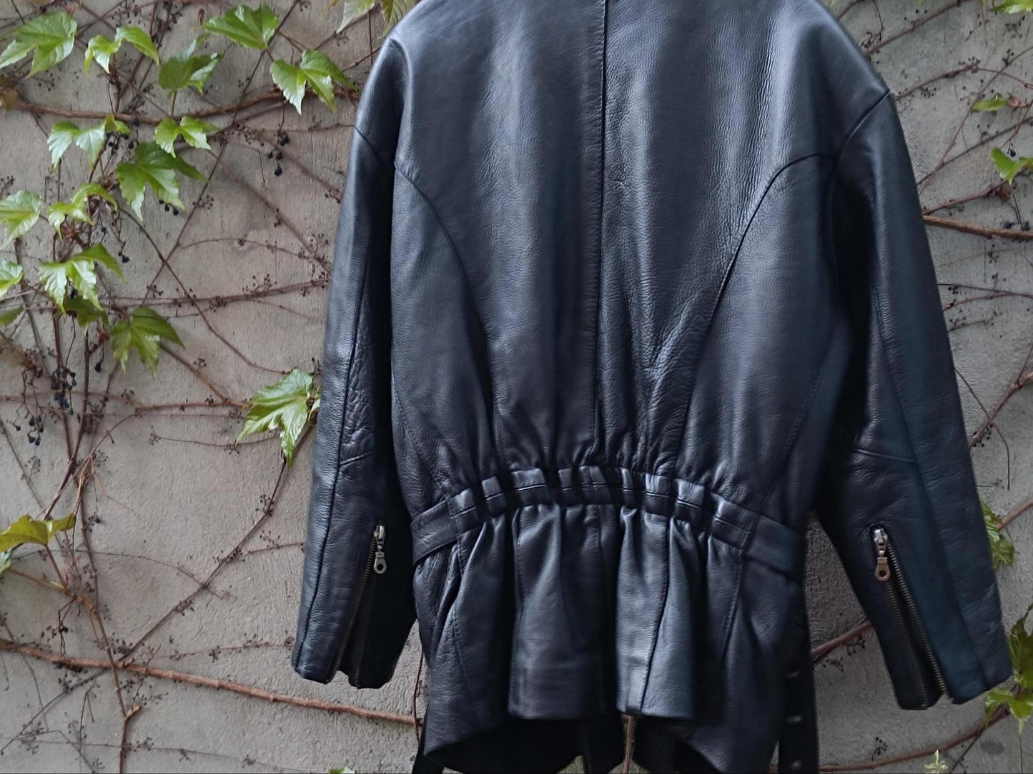 Authentic vintage leather biker coat inspired by rock and roll style, this is an image of a unisex Moto jacket from the 80s.This image is taken from the back and focuses on the rouched details