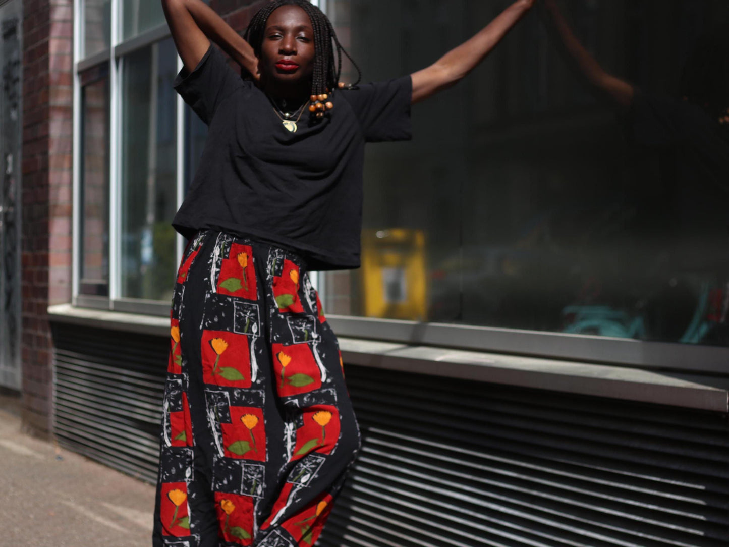 A 90s Retro floral maxi skirt in motion as the model shifts stance, showcasing the soft flow of the vintage fabric and vibrant red and orange hues under bright daylight.