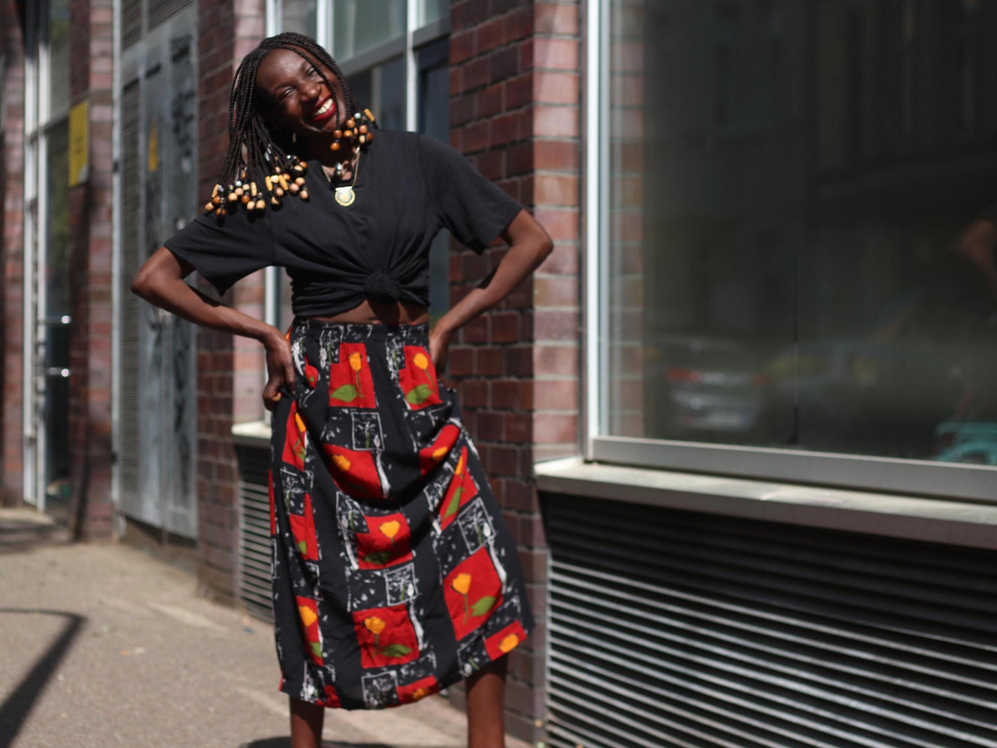 A retro 90s floral maxi vintage skirt in motion as the model shifts stance, showcasing the soft flow of the vintage fabric and vibrant red and orange hues under bright daylight.
