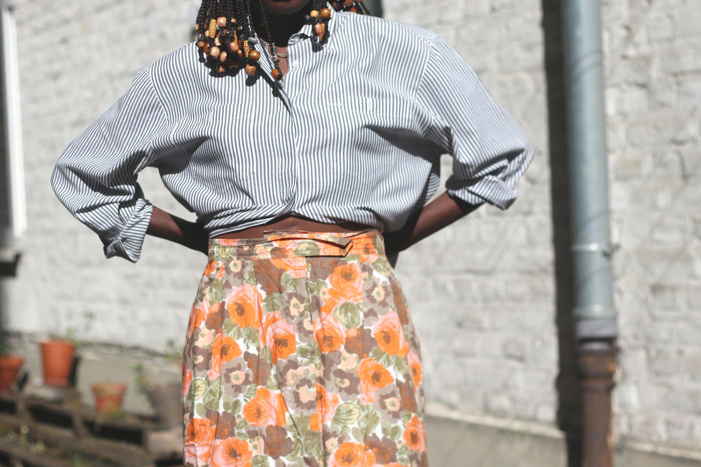close-up of an 80s floral orange skirt on a female model wearing the bold design with a pinstriped button-up shirt outdoors against a sunlight white bricked wall