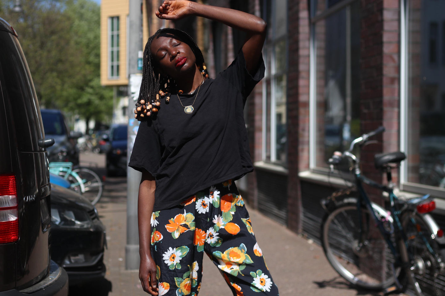 An artistic portrait of a model with beaded braides, wearing a pair of vintage boho floral capris with black t-shirt, with her eyes closed, hands raised to the sun she exudes a carefree spirit perfect for summer festivals