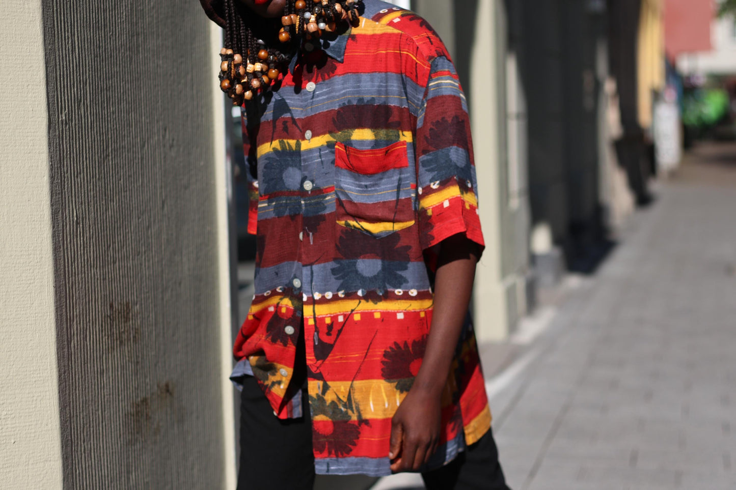 Close-up image of female model in a vintage Montino tropical floral shirt with bold island print styled with black pants photgraphed in an urban setting with buildings and cars in the background, highlighting short sleeves, 90s unisex fit, and bold summer tones.
