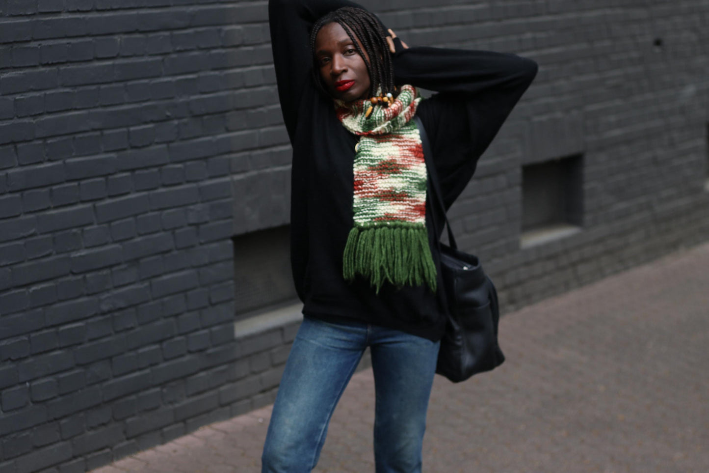 Unisex boho knit scarf with long tassels and a warm, chunky feel, styled on a female model wearing g jeans and a black sweater, captured against a grey bricked wall
