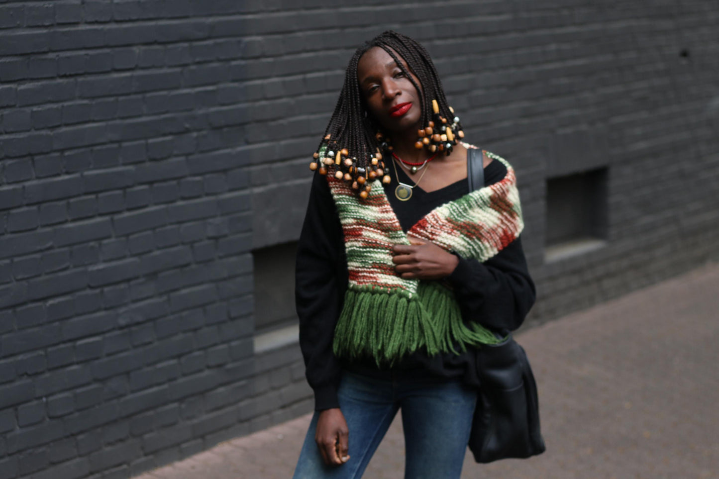 Colorful handmade scarf with statement tassels and a retro vibe, perfect for cold weather fashion showcased on a female model with beaded braids , a black sweater and oversized handbag