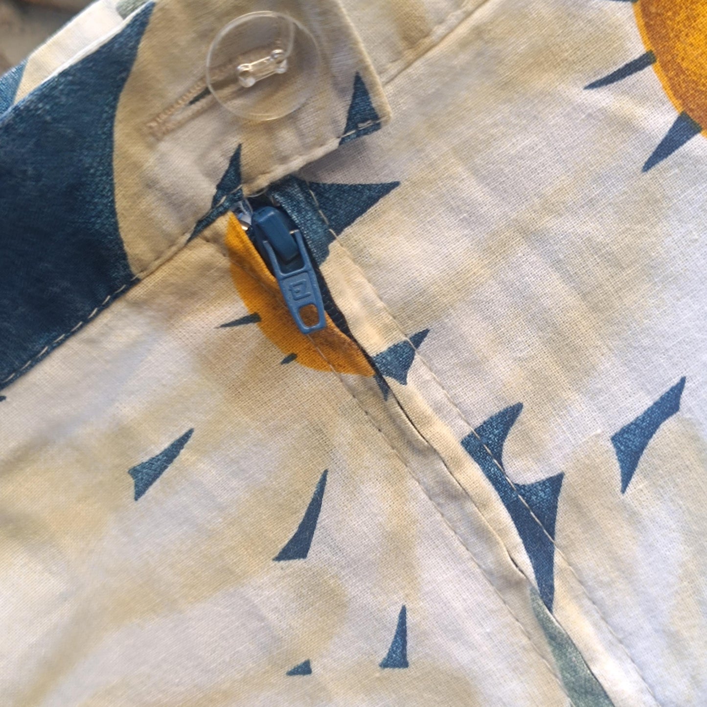 A close-up image of a skirt with a vibrant floral design, featuring large white daisies with yellow centers and blue petals, focus is on the button and zipper