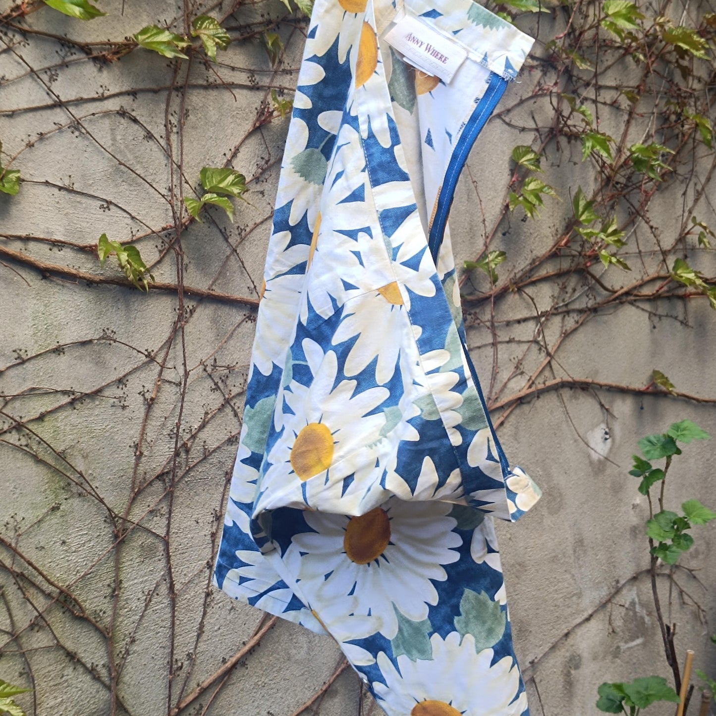 90s vintage blue and White Floral Print Skirt with a bold daisy print hanging on a clothing line in the garden against a walled background with browning ivy and twines