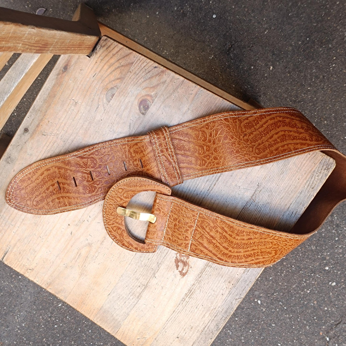 Handmade Vintage 70s retro fashion leather belt with an oversized silhouette photographed on a rustic brown wooden chair. The image showcases the leather belt's unique grain pattern