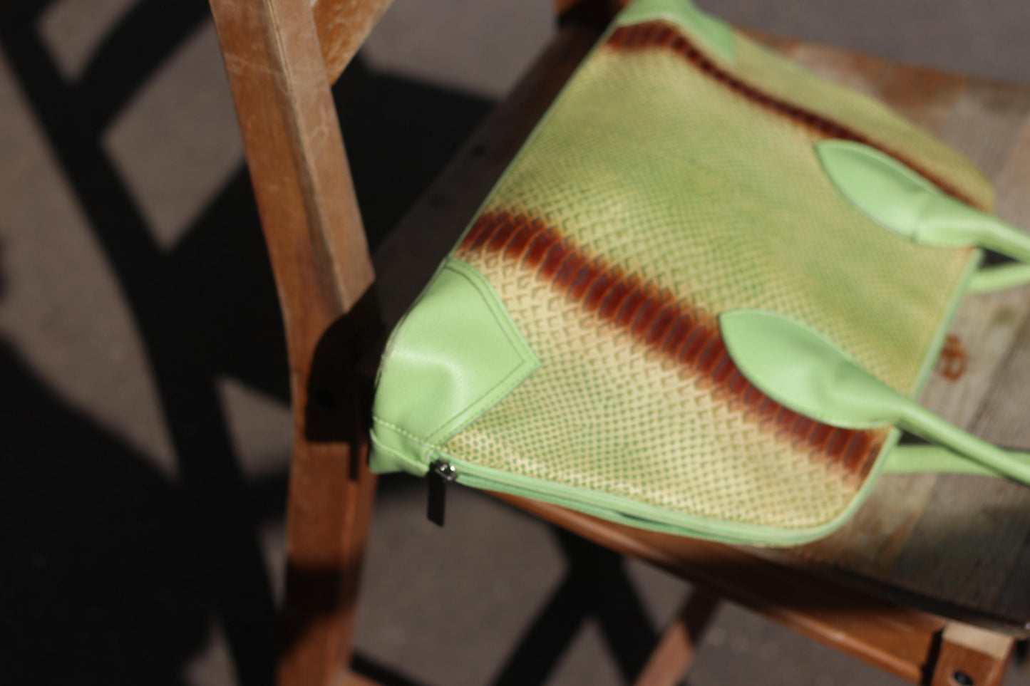 A close-up side view photo of an 80s vintage, light green faux leather handbag with an animal print stripe. The picture focuses on the edges of the bag while it rests on a wooden chair with a slatted back.