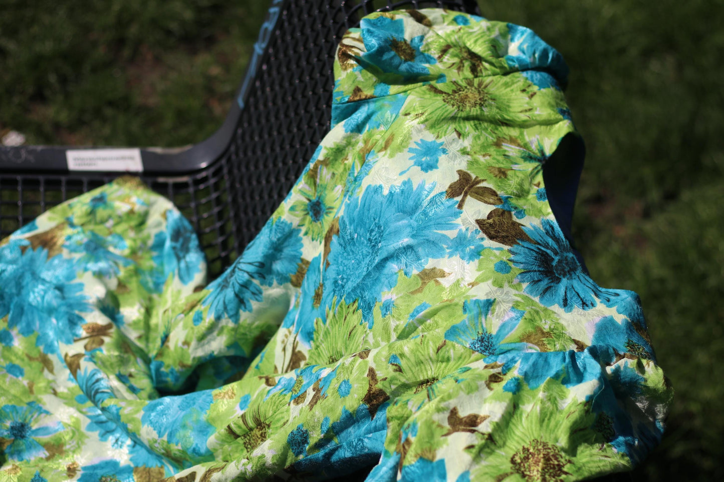 An artistic flat lay image of a vintage 70s Floral Dress photographed resting on a green steel bench outdoors
