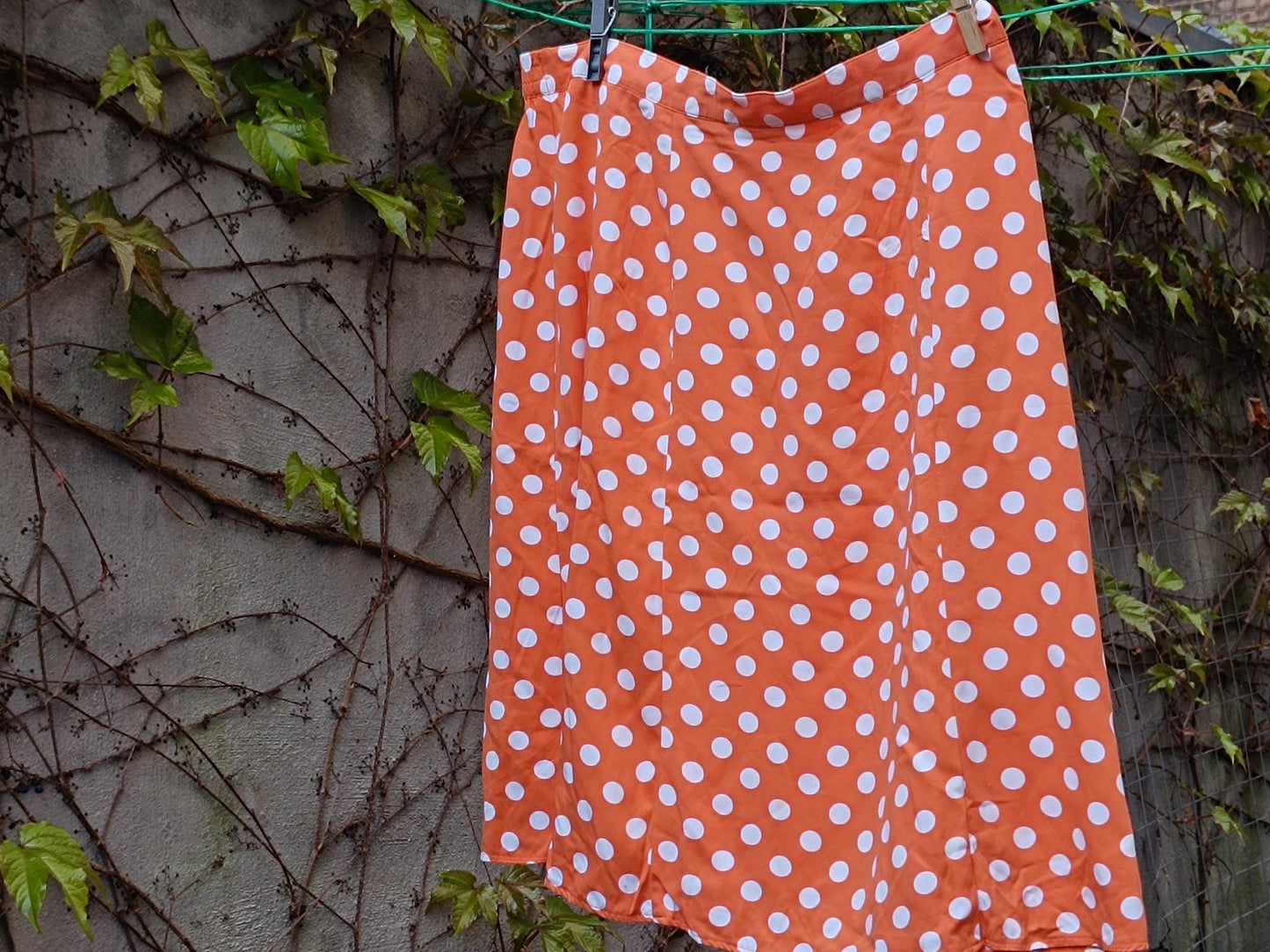 A still life image of a Chic French Flair 90s Polka Dotted Skirt in Orange. The vintage Flirty Mini design is hanging on a clothing line with two clothing pegs. the vibe is dreamy Parisian chic holiday feel