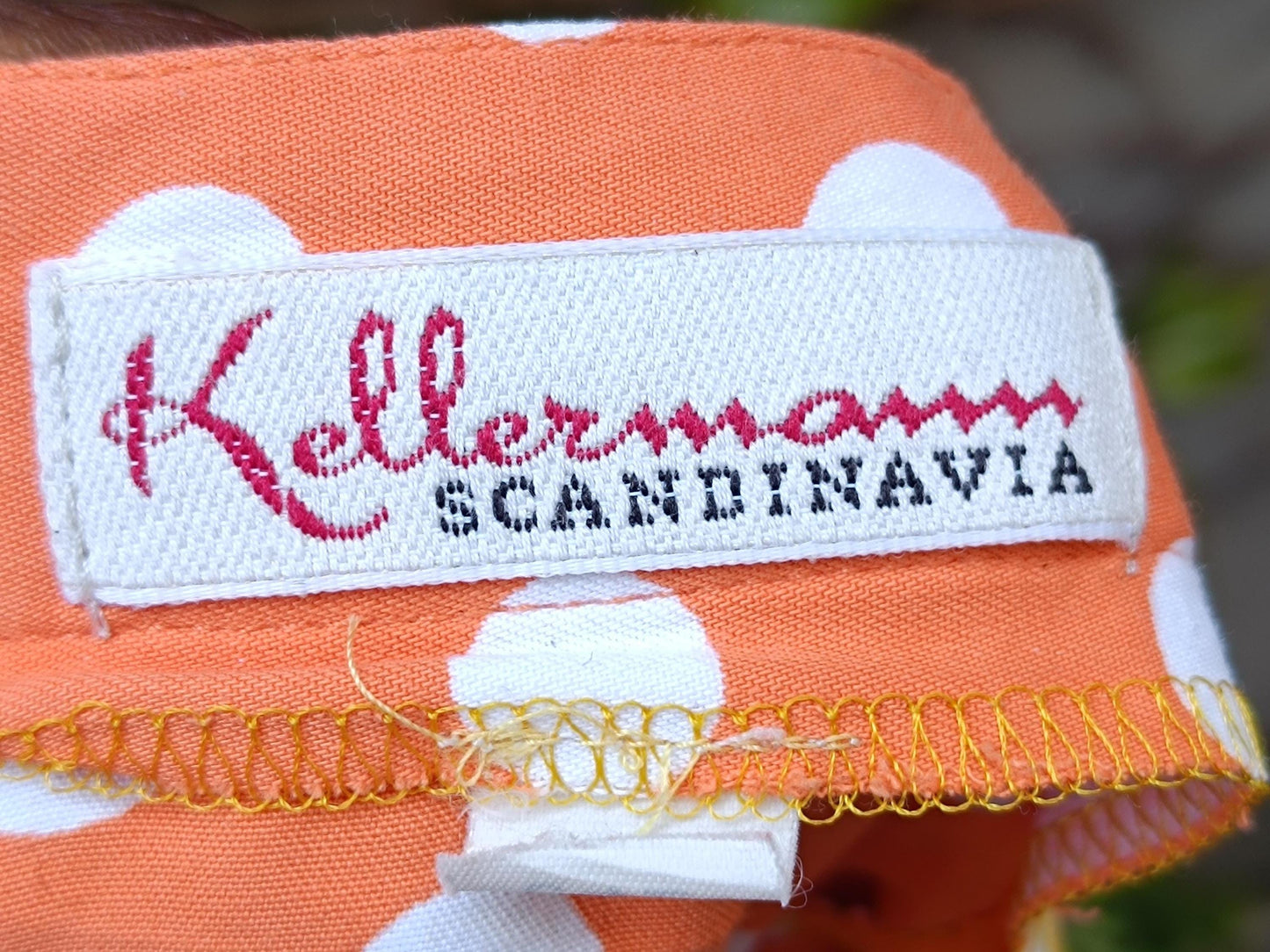 An image of the brand label for a Chic French Flair 90s Polka Dotted Skirt in orange. The label is white with red and black lettering and reads " Kellermanm Scandinavia"