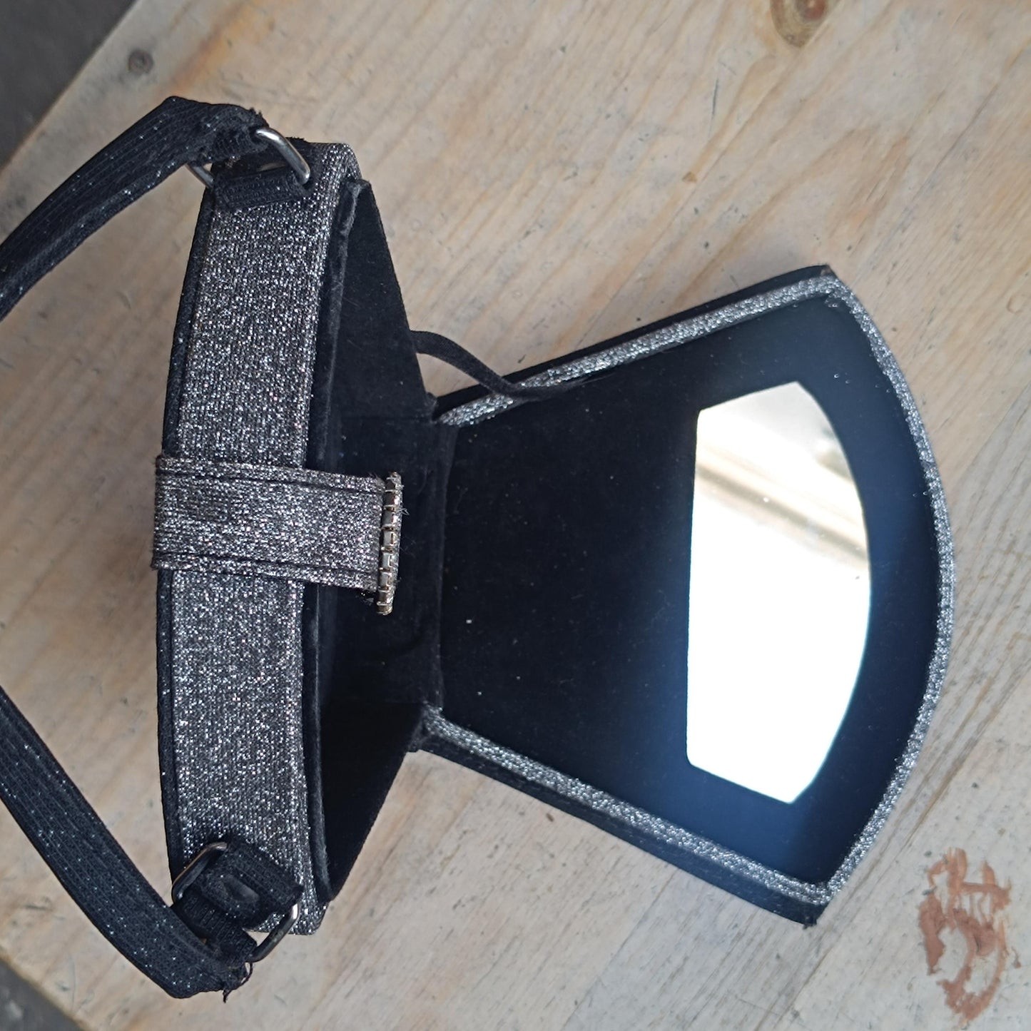 Vintage black glitter mini bag with top handle and faux-bling detail, laid flat and open on a wooden surface .The small mirror inside the y2k bag is visible