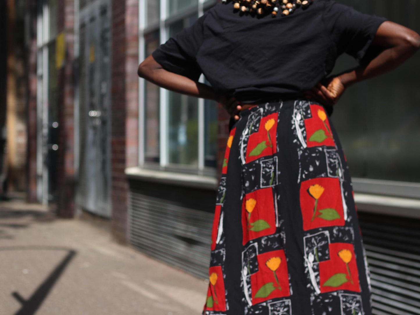Zoomed in image of a Back view of a female model in a flowy retro red vintage skirt with floral print, highlighting the contrast between matte black sections and vibrant retro flower prints.