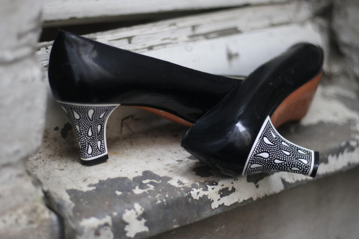 Detailed view of the statement heels of Italian-made black court pumps shot on a brown rustic surface. The focus is on the black and white teardrop print on the heels