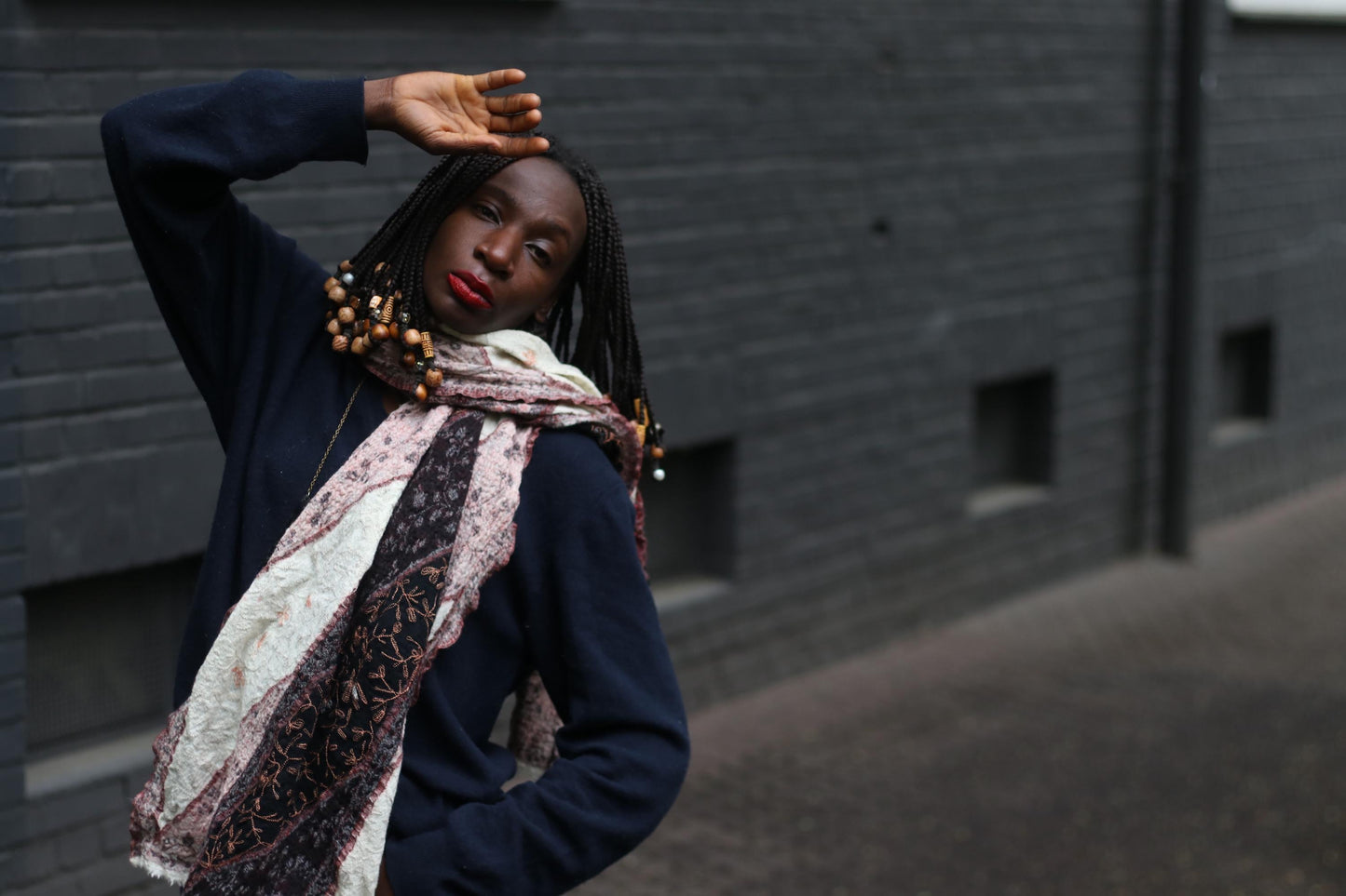 A vintage boho retro patterned scarf worn as by a female model in front of a textured brick wall. The model showcases the unique print and color palette of the 90s oversized scarf.