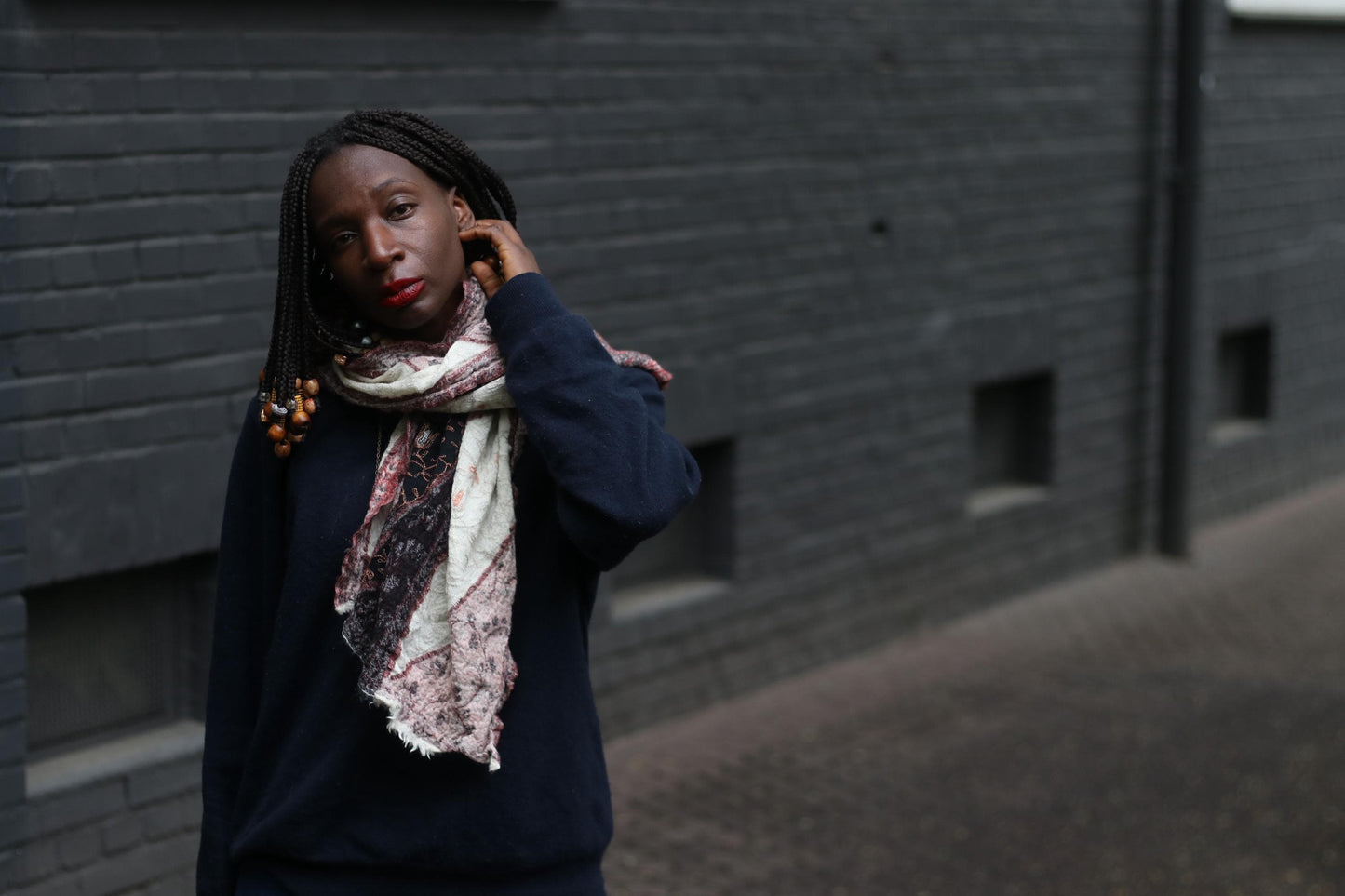 A female model in a boho chic multicolored scarf standing in front of a grey brick wall
