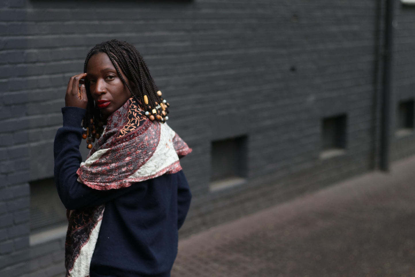 side view of a retro patterned scarf worn by a female model, in front of a grey textured brick wall. The image highlights the unique print and color palette of the boho oversized scarf.
