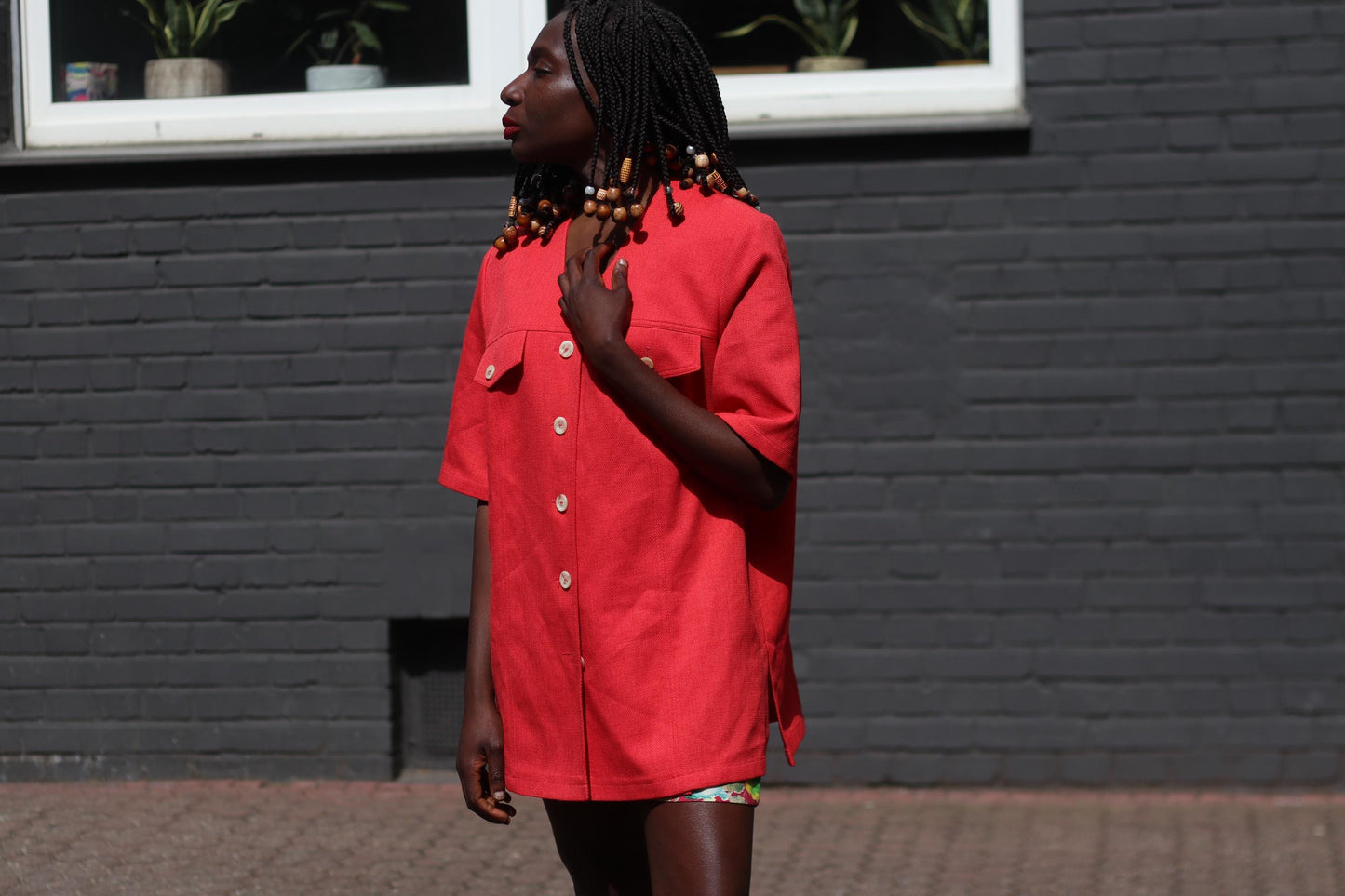Female model wearing a vintage 90s Short-Sleeve Blazer by Mark Wald as an oversized mini dress photographed in front of a grey brick wall. The image showcases the bold V-Neck Jacket as a lightweight choice for suiting up in the summer