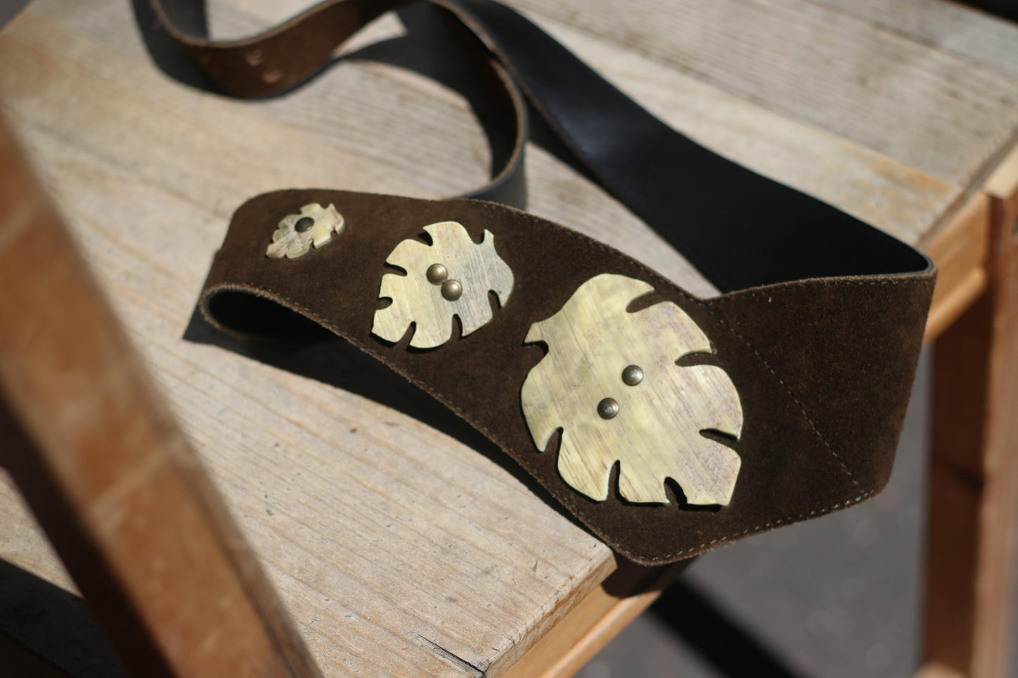 Traditional Vintage Austrian Suede belt with decorative brass details photographed on a brown rustic chair outdoors .