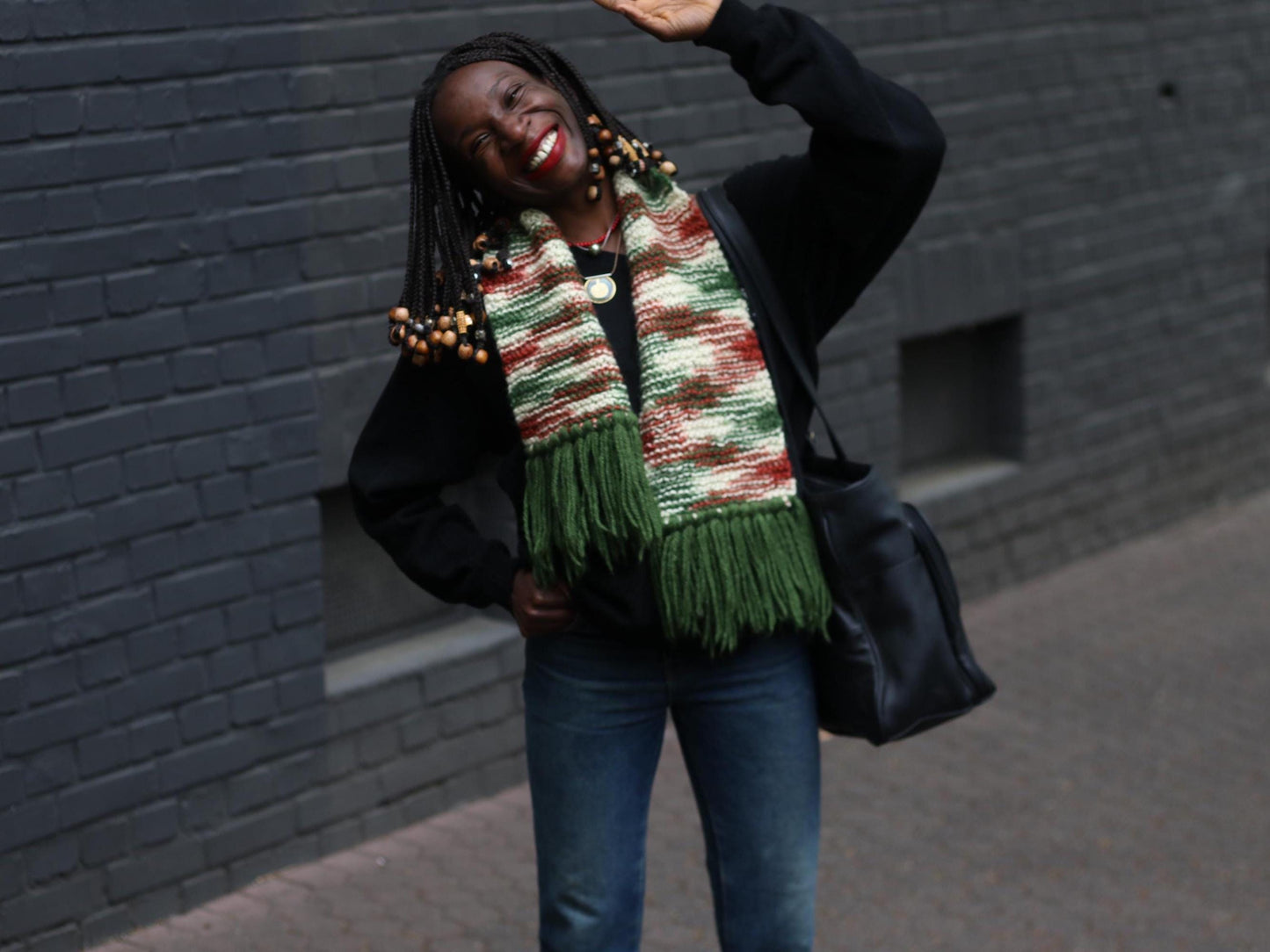 Handmade vintage green knit scarf with chunky tassels worn by a smiling woman standing against a brick wall