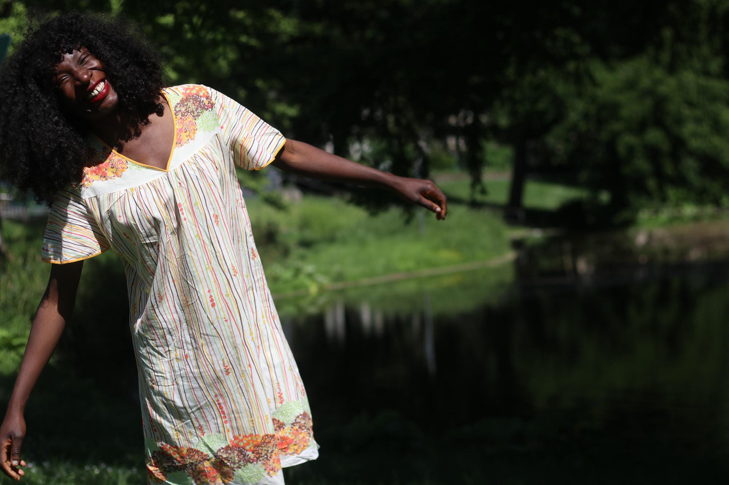 Full-length view of vintage dress on a model with black hair in natural light outdoors shot in front of a body of water with trees and grass in the background