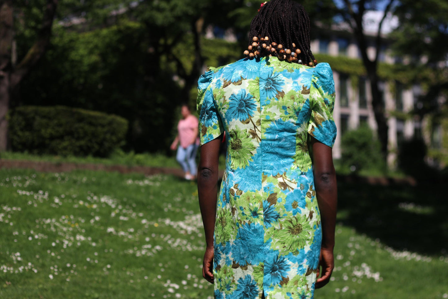 The back view of a vintage cottagecore-style dress on a model with beaded braided hair. the dress features bold floral patterns and retro puff sleeves and is perfect for spring or summer wear.