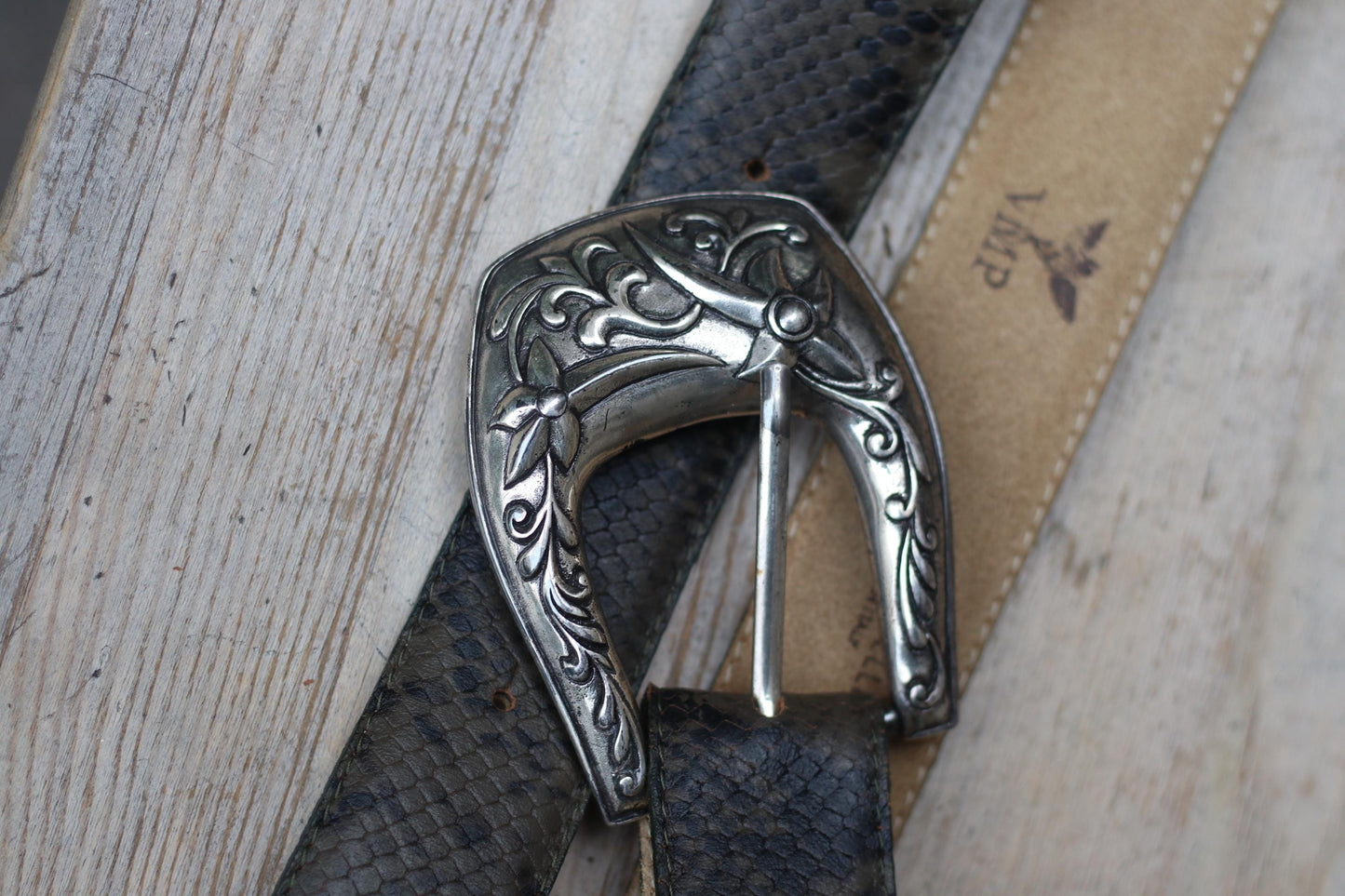 Overhead shot of a vintage tooled snakeskin-embossed 70a western belt with an ornate silver buckle, flat on a light wooden surface