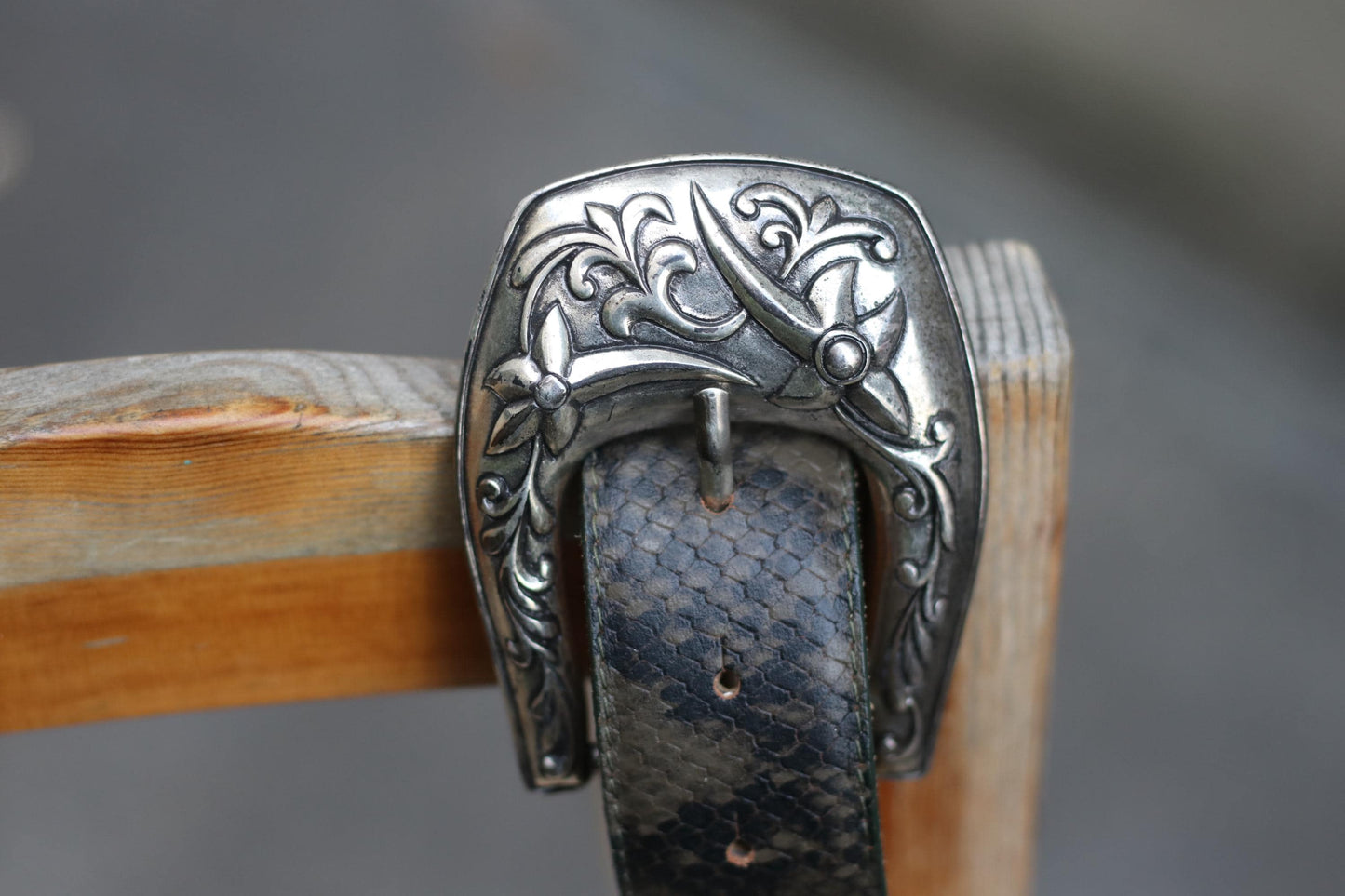 Detailed image of a vintage 70s tooled belt with an ornate silver western buckle with intricate floral and scroll engravings.