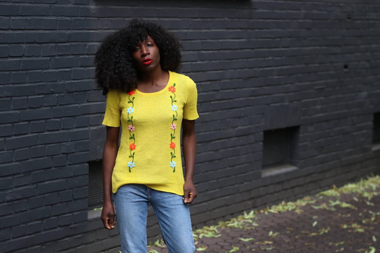 Retro-style vintage yellow top with vertical flower embroidery, styled with denim jeans in a candid street-style photo.