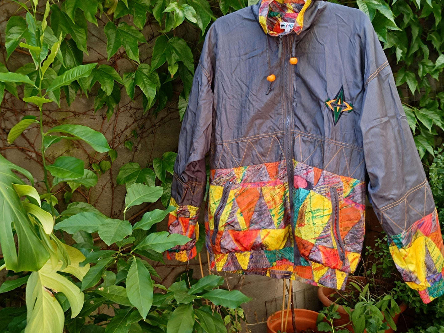 Bold color block vintage 90s jacket photographed hanging from a clothing line outdoors against a leafy green backdrop